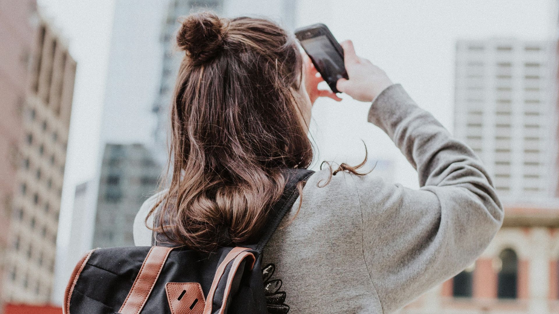 woman taking photo of high-rise building beside road