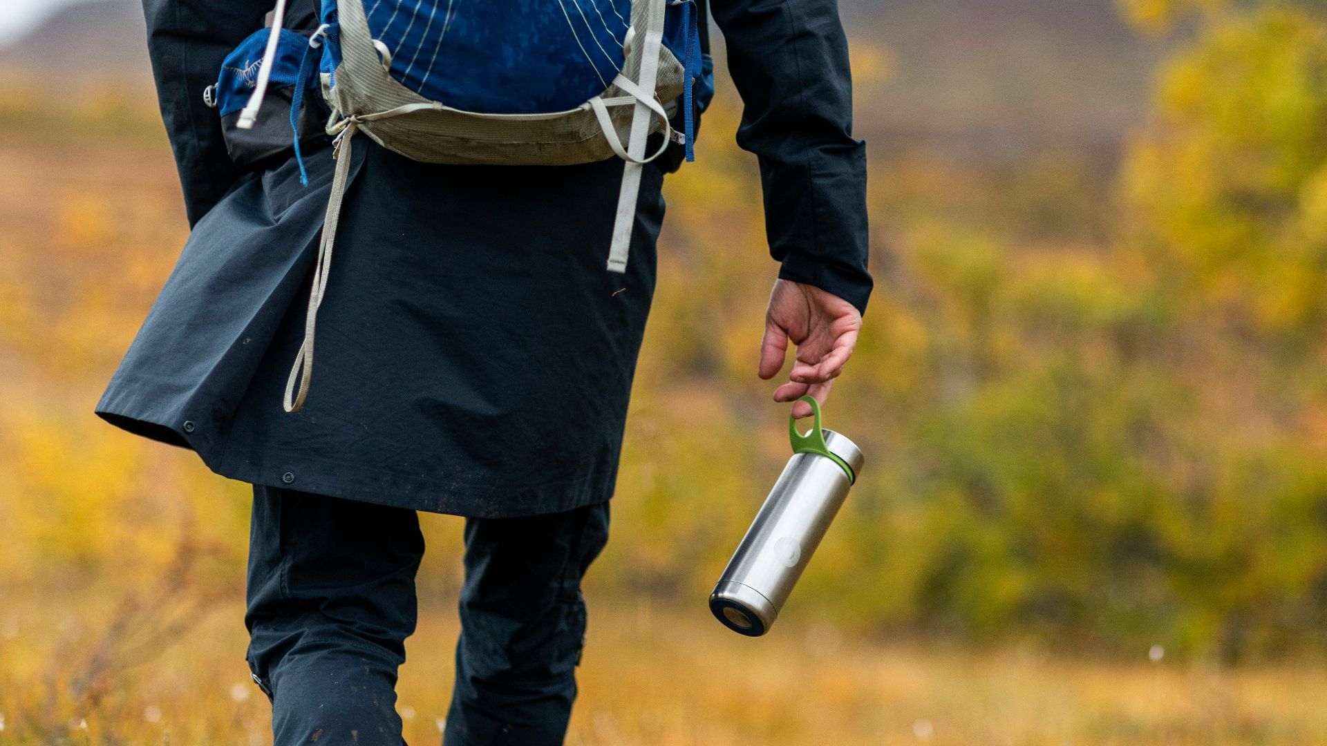 person in blue and white striped shirt and black pants holding white and silver travel mug