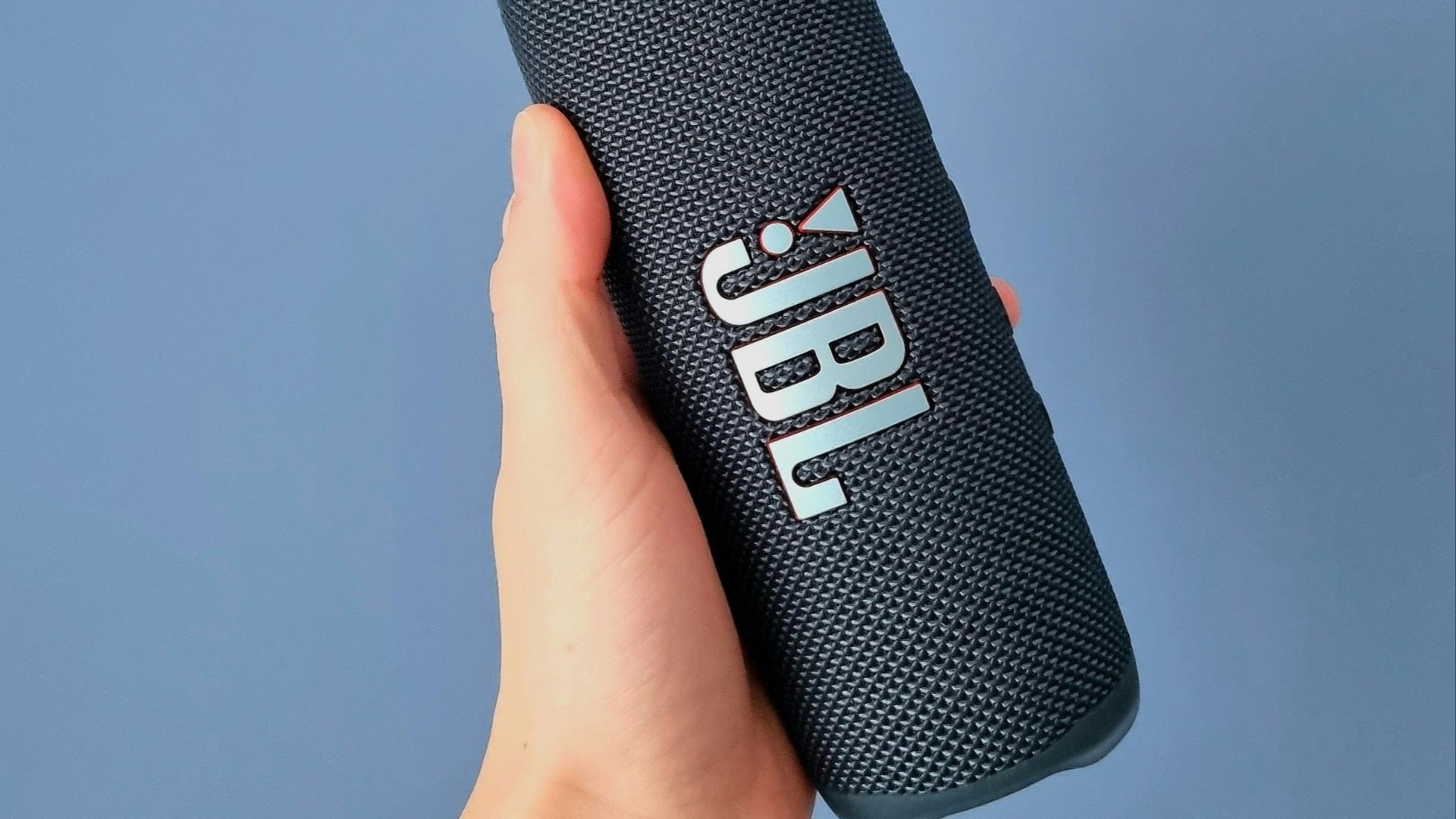 a hand holding a bluetooth speaker against a blue background