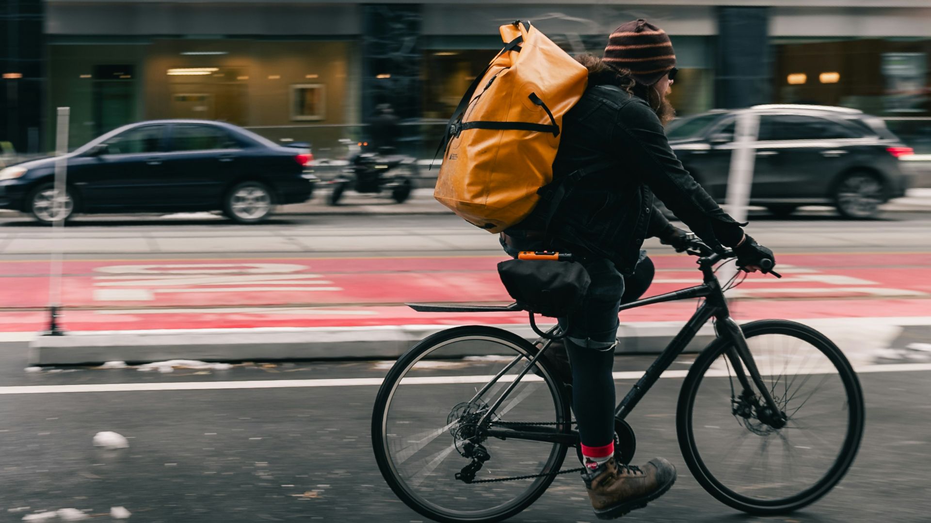Man with large yellow backpack rides bicycle on city street