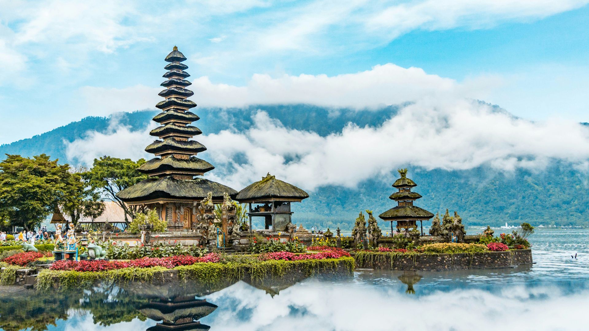 brown and green temple near body of water under blue and white cloudy sky during daytime