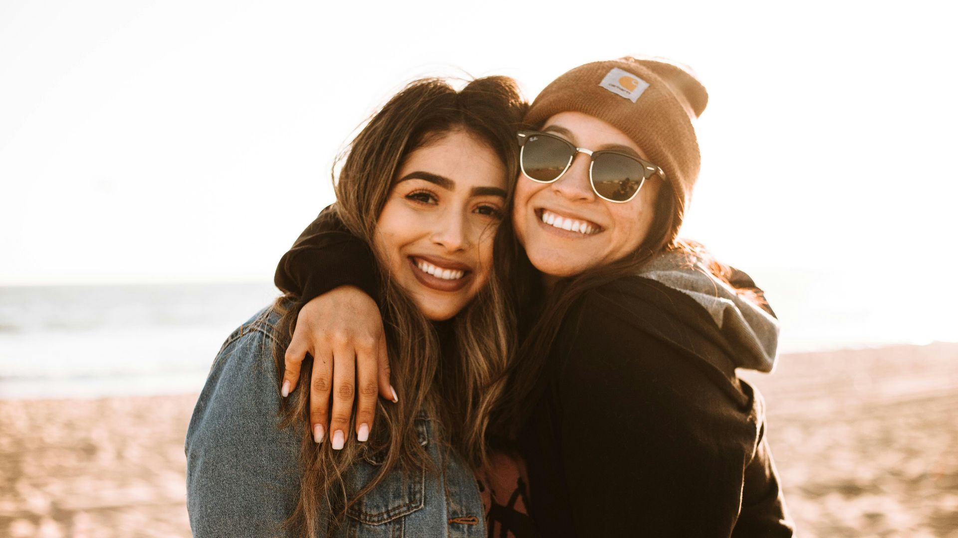 woman hugging other woman while smiling at beach