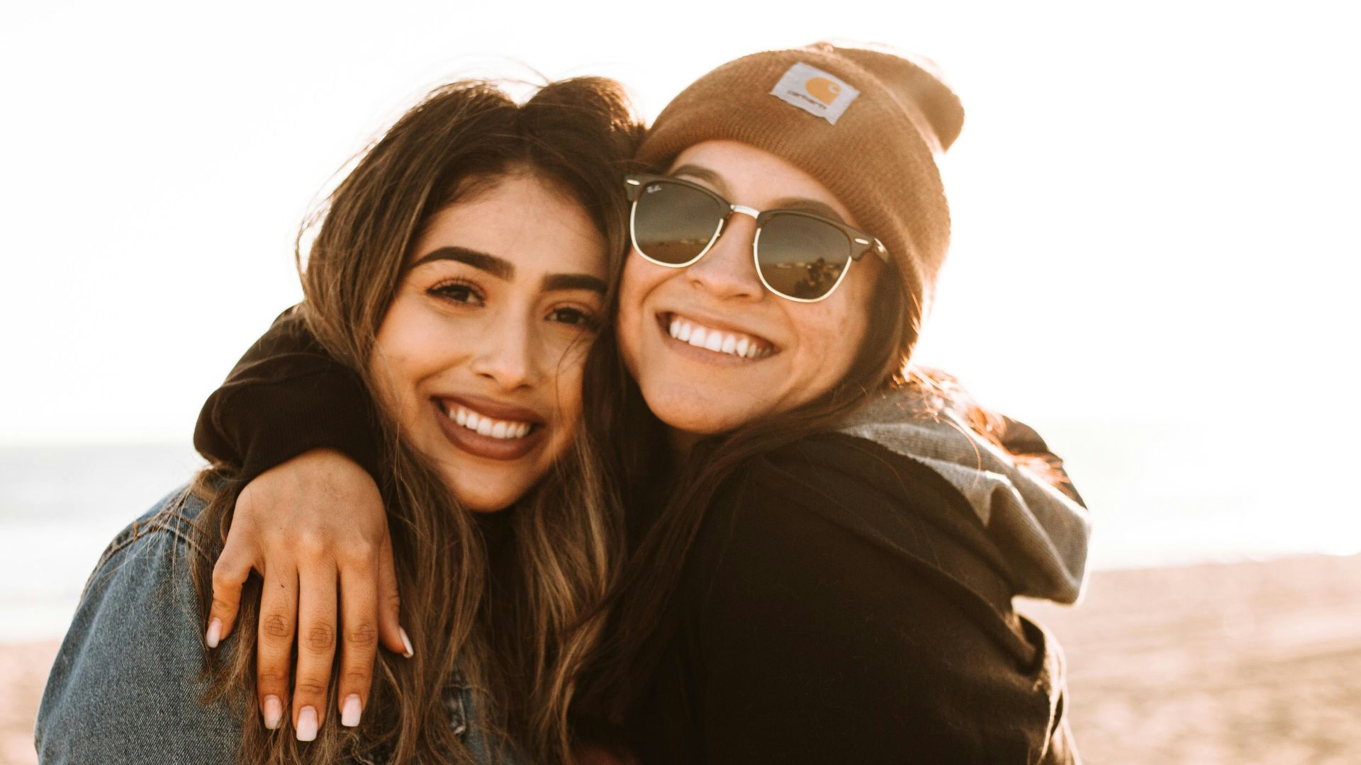woman hugging other woman while smiling at beach