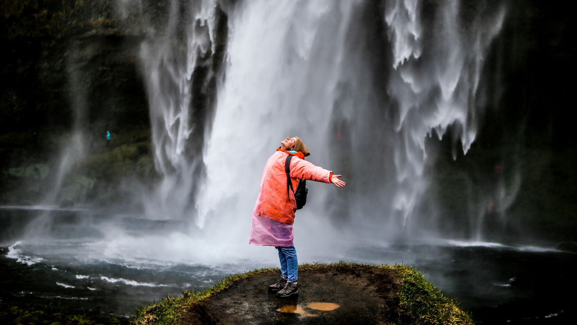 woman in blue jacket standing on rock near waterfalls during daytime
