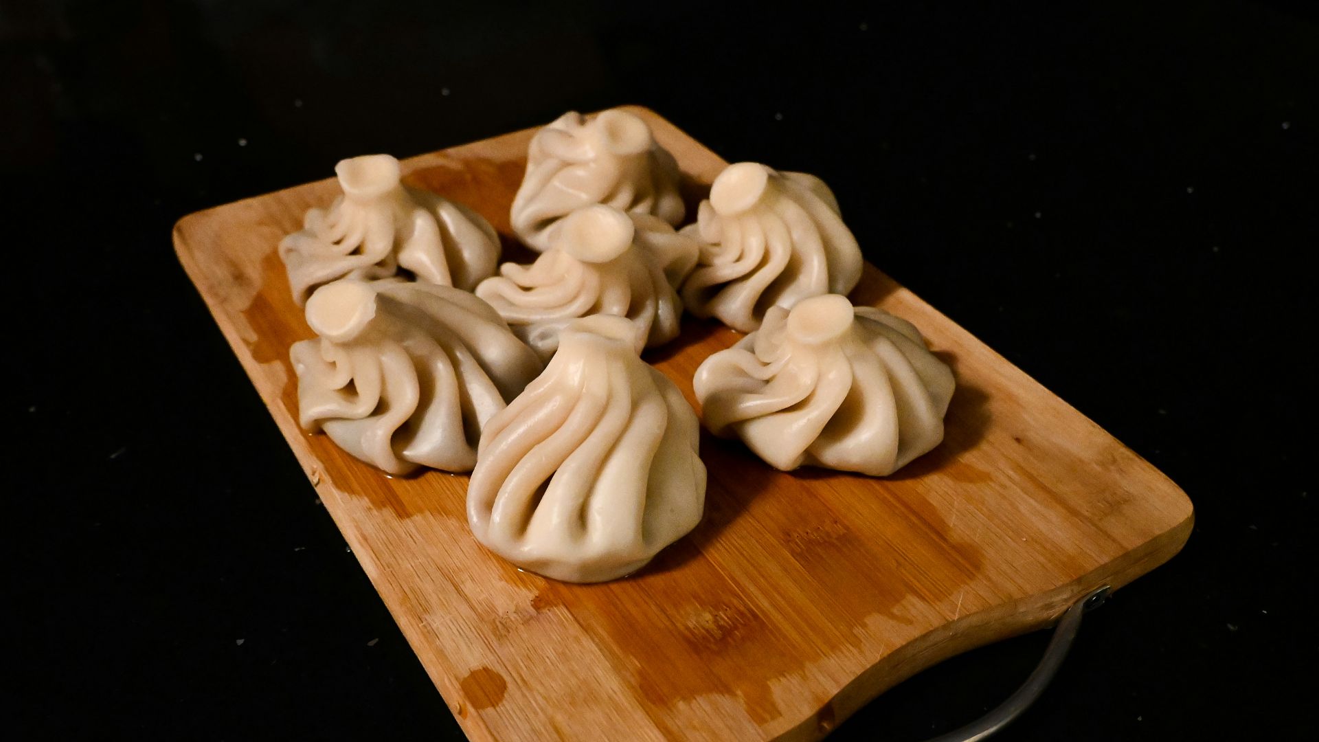 a wooden cutting board topped with dumplings on top of a table