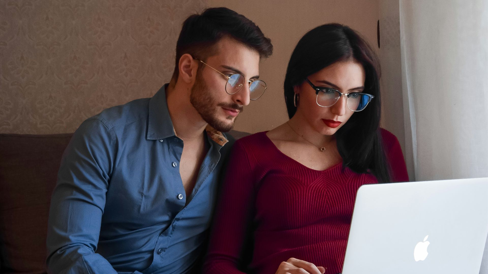 A man and woman sitting on a couch looking at a laptop