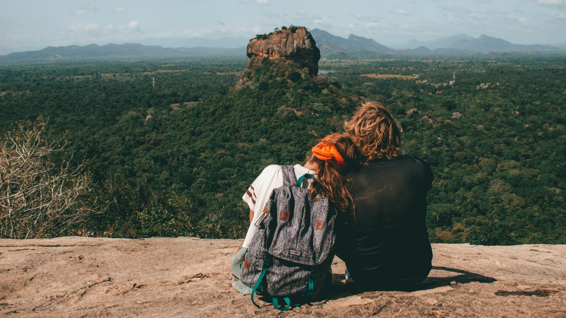 man and woman sitting beside cliff