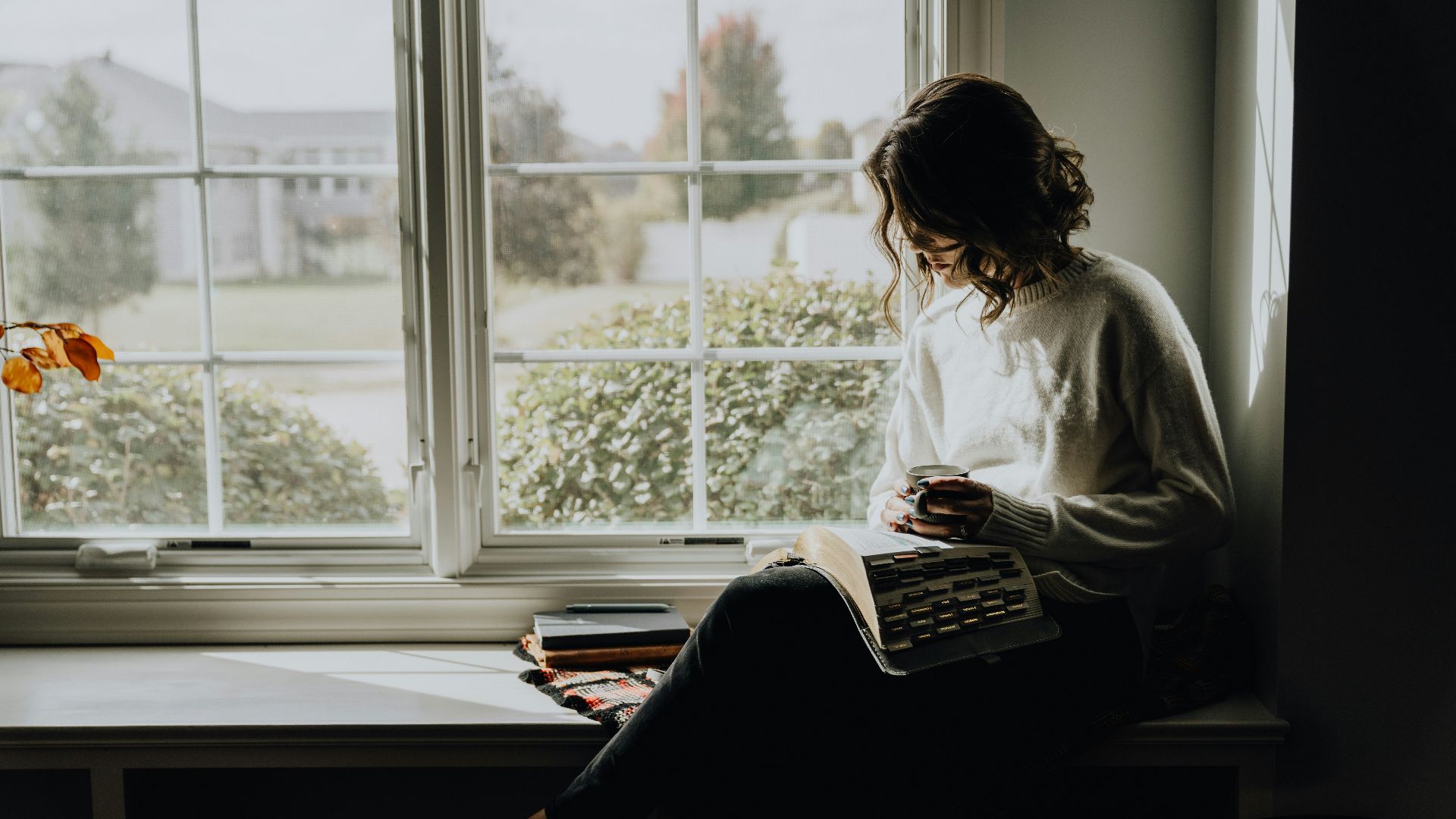 A woman sitting on a window sill reading a book