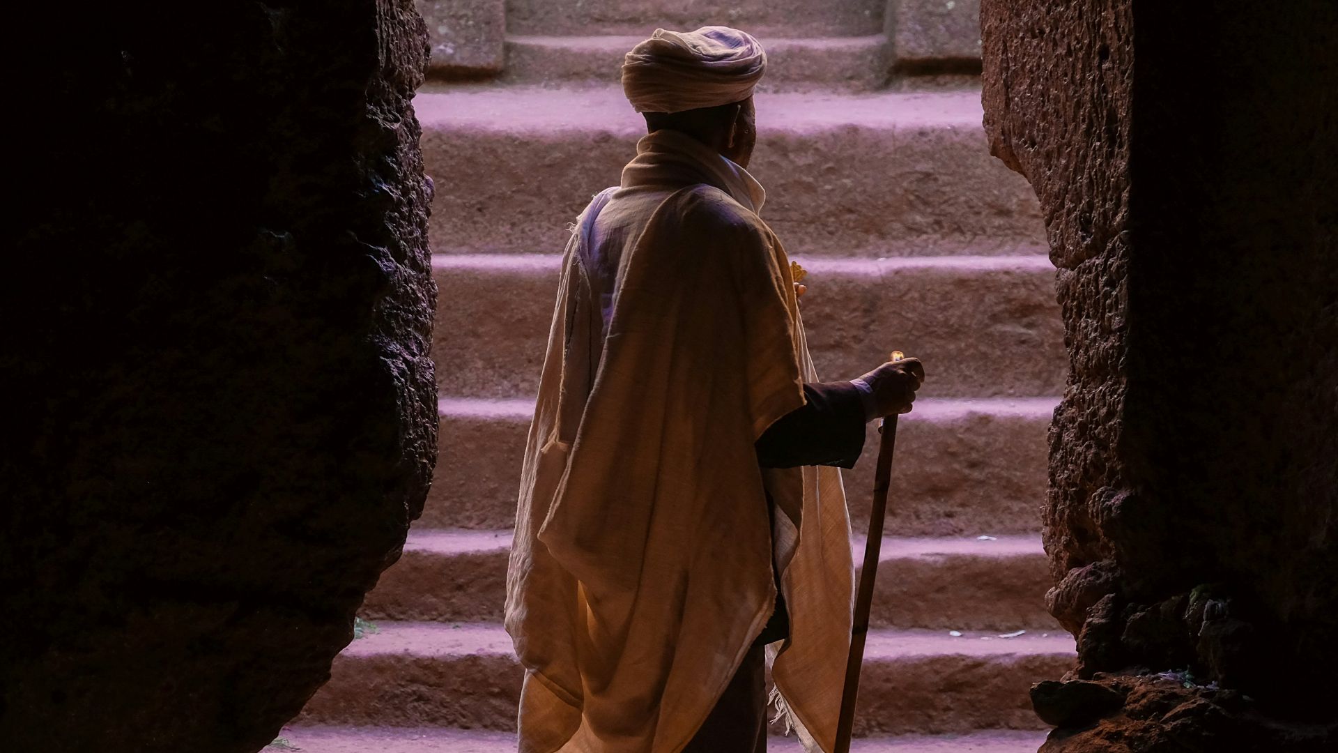 man standing on brown stone cave entrance while holding cane