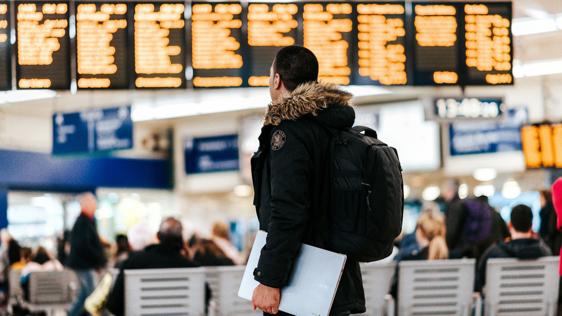 man standing inside airport looking at LED flight schedule bulletin board