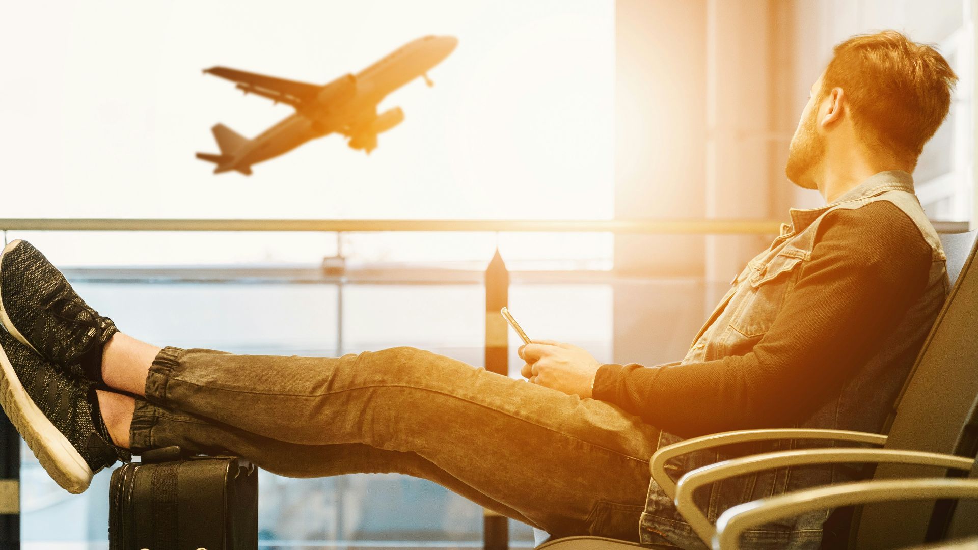man sitting on gang chair with feet on luggage looking at airplane