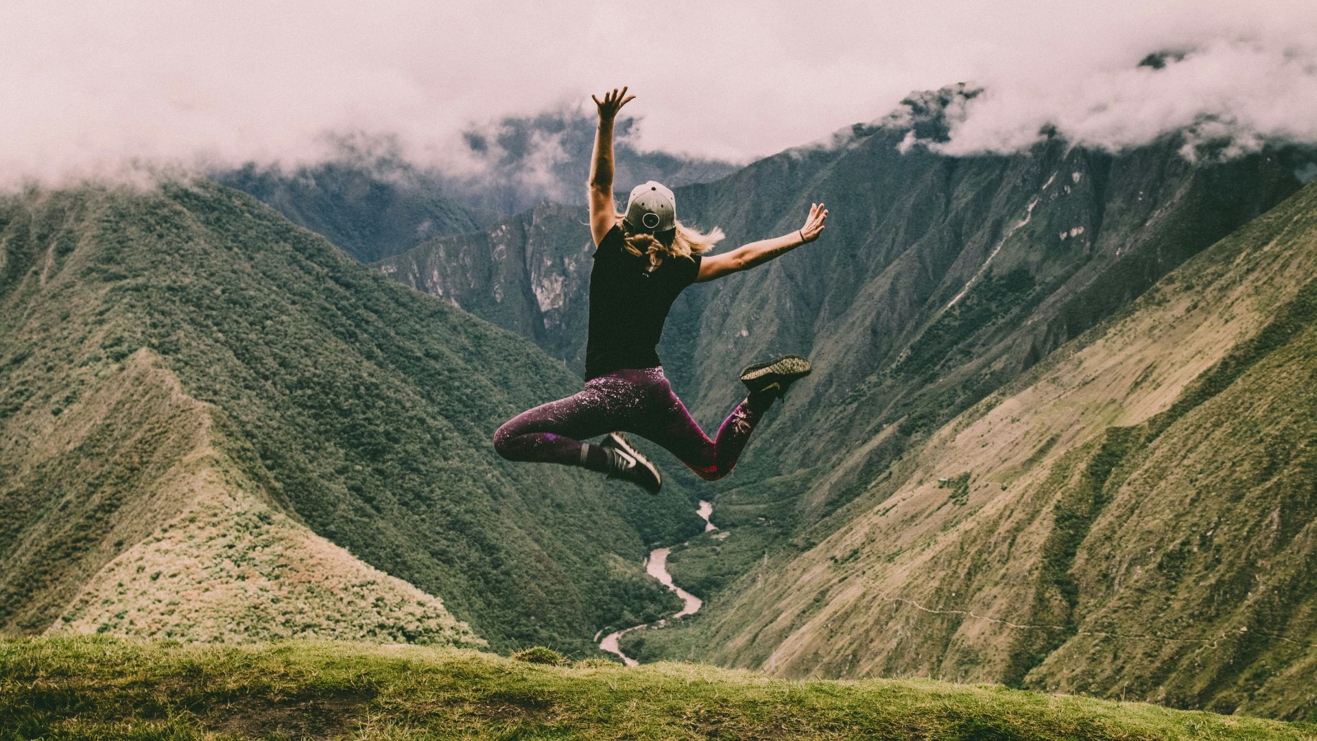 woman jumping on green mountains
