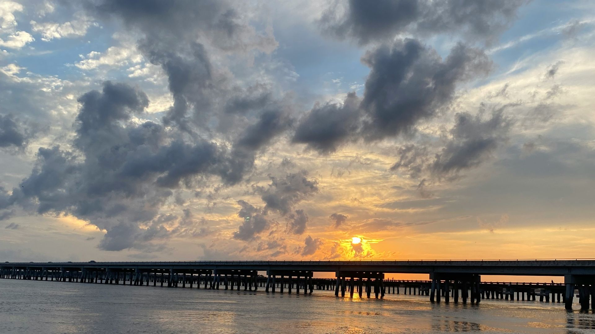 the sun is setting over the ocean with a pier in the distance