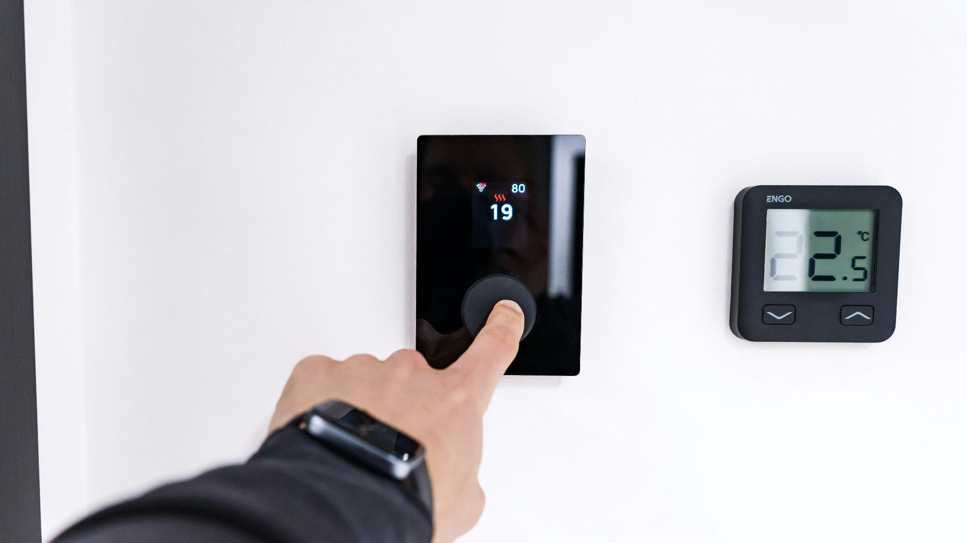 Finger adjusting a modern digital thermostat on wall