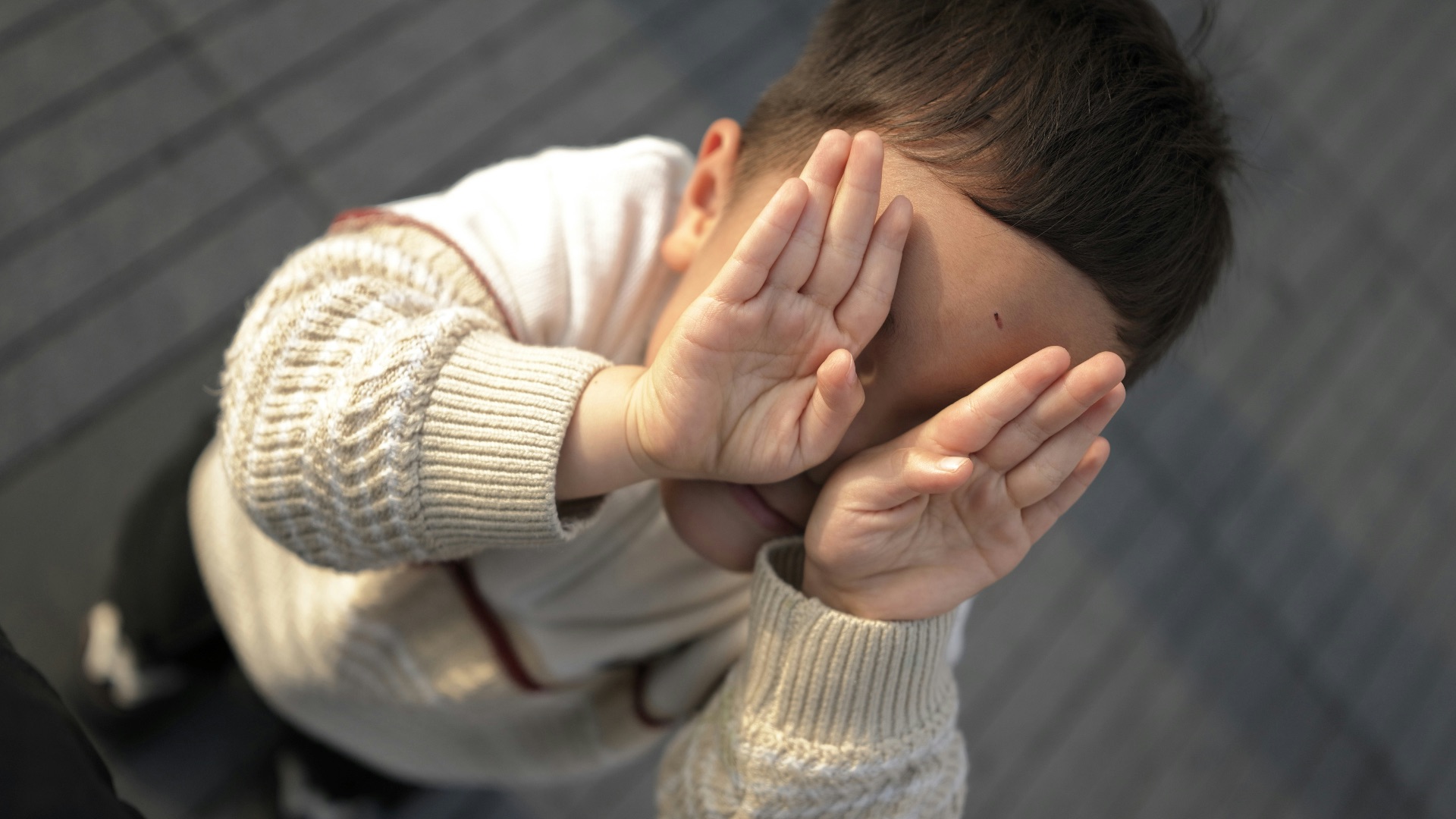 A young child covers their face with hands.
