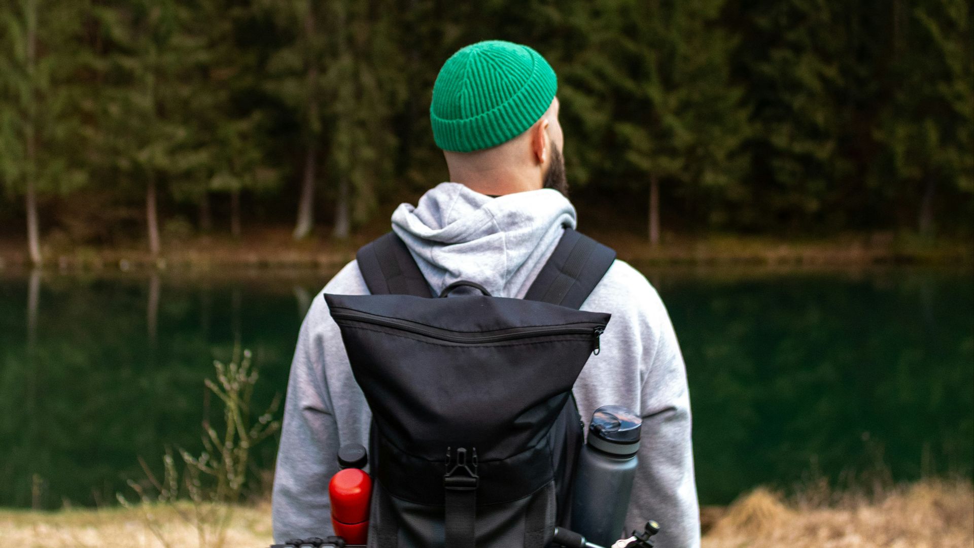 Man stands near a lake with a forested background.