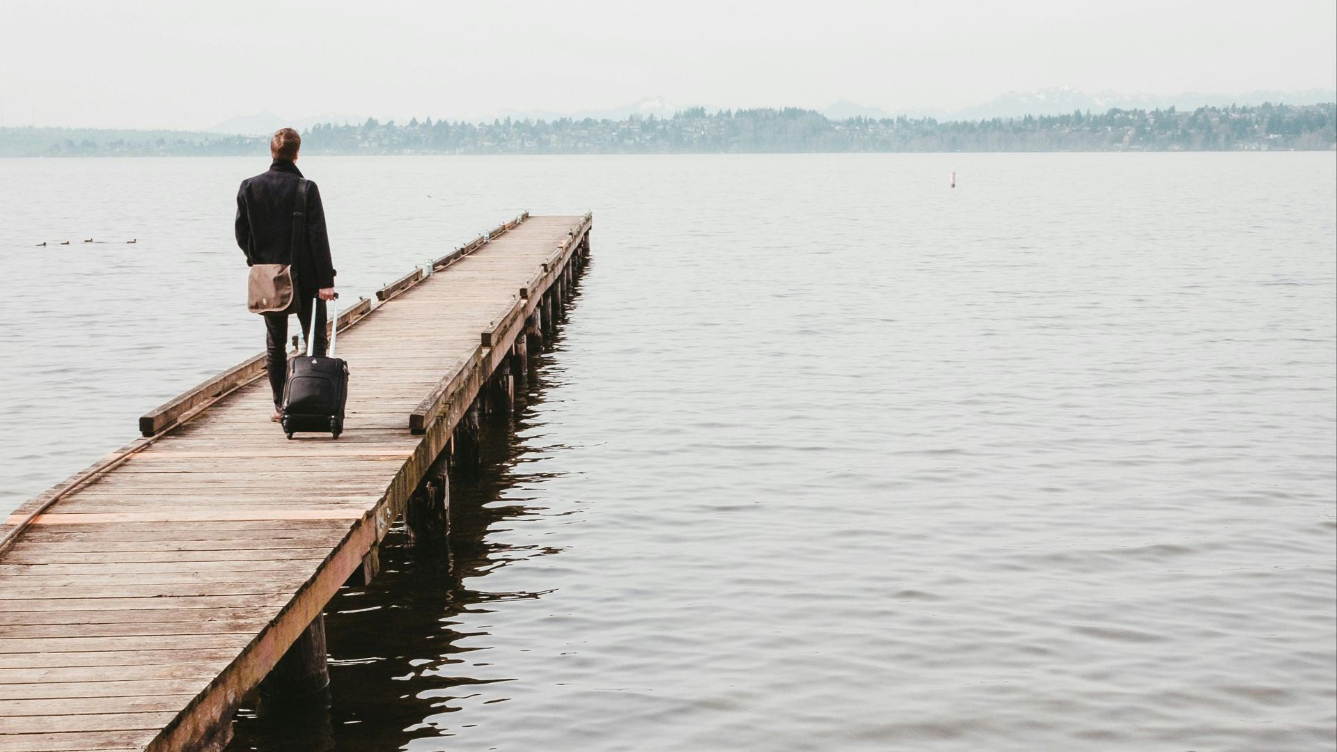 person walking on dock while towing luggage bag