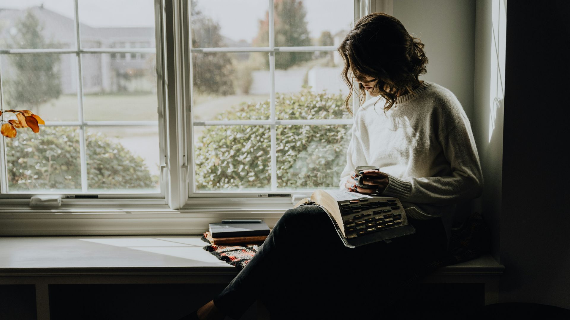 A woman sitting on a window sill reading a book