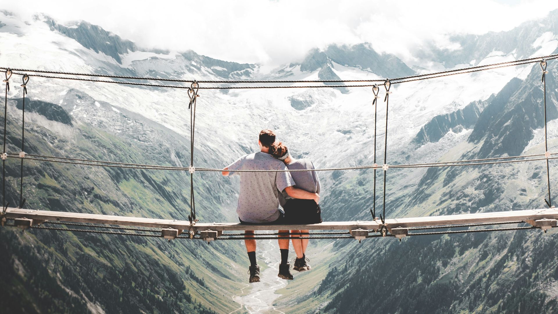 man and woman sitting on hanging bridge at daytime