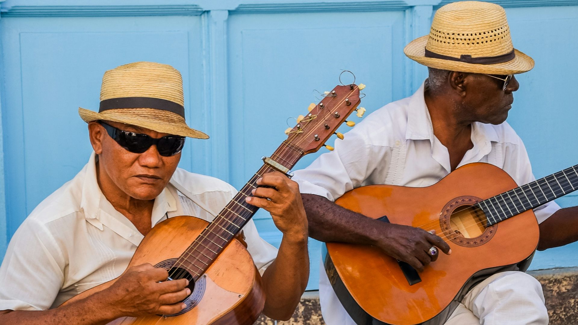 two men sitting on a bench playing guitars