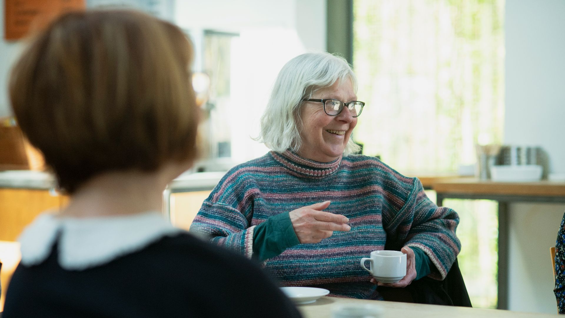a woman sitting at a table talking to another woman