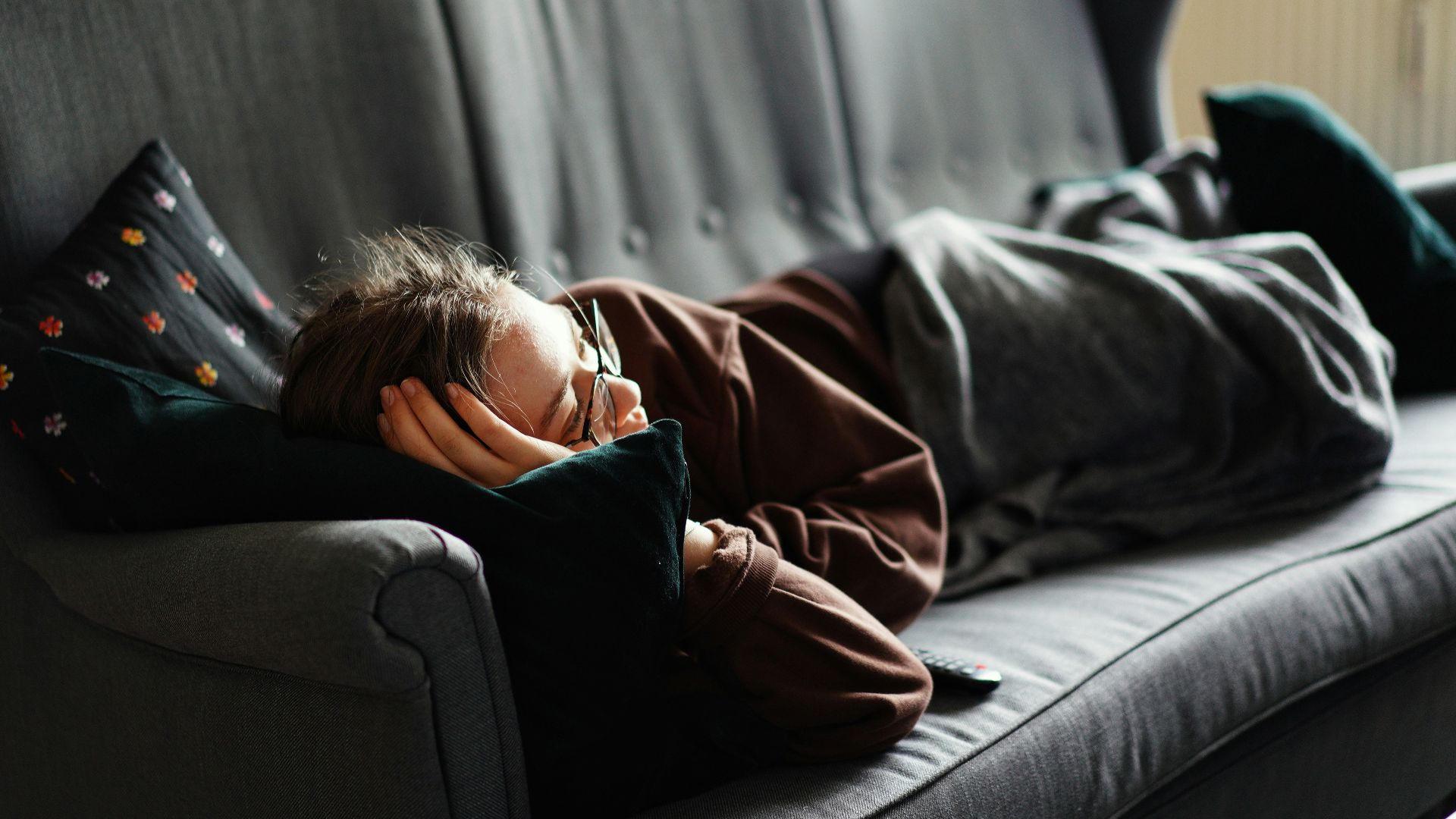 woman in pink jacket lying on gray couch
