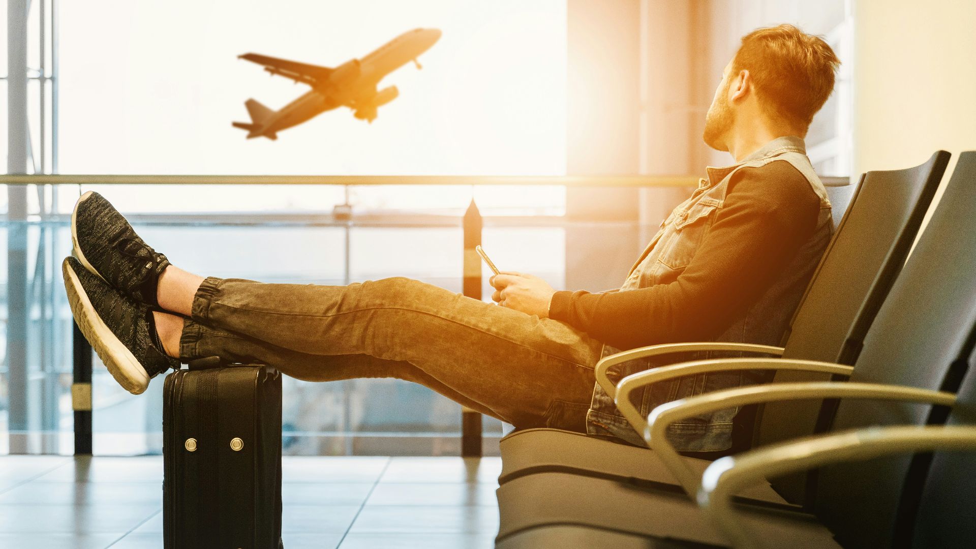 man sitting on gang chair with feet on luggage looking at airplane