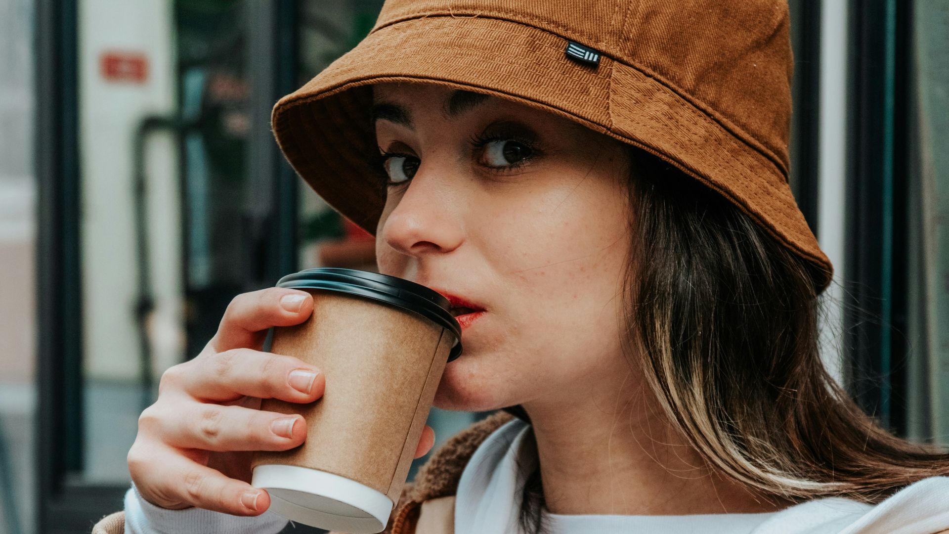 woman in brown coat holding white ceramic mug