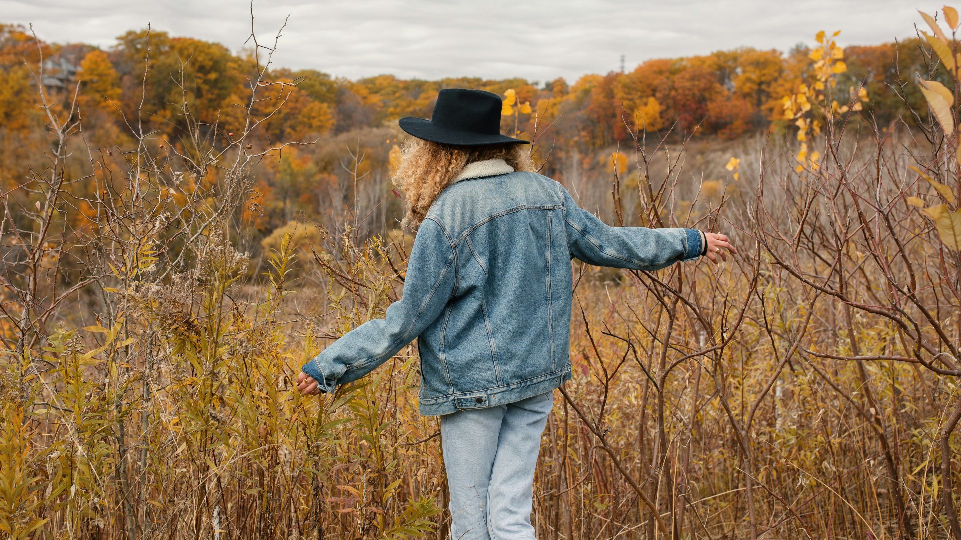 woman wearing blue jacket walking towards the brown grass