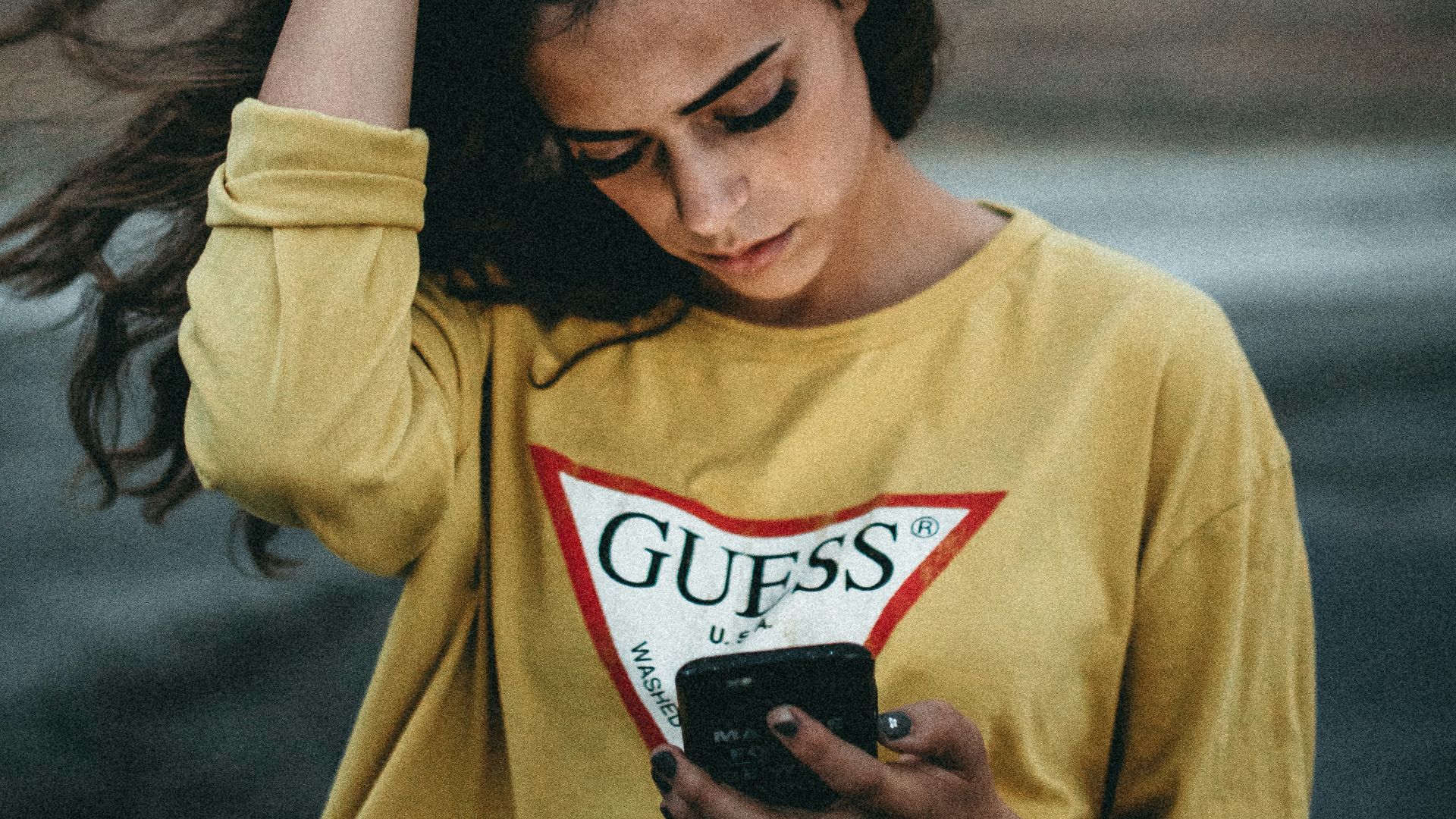 woman looking at her phone with right hand on her head