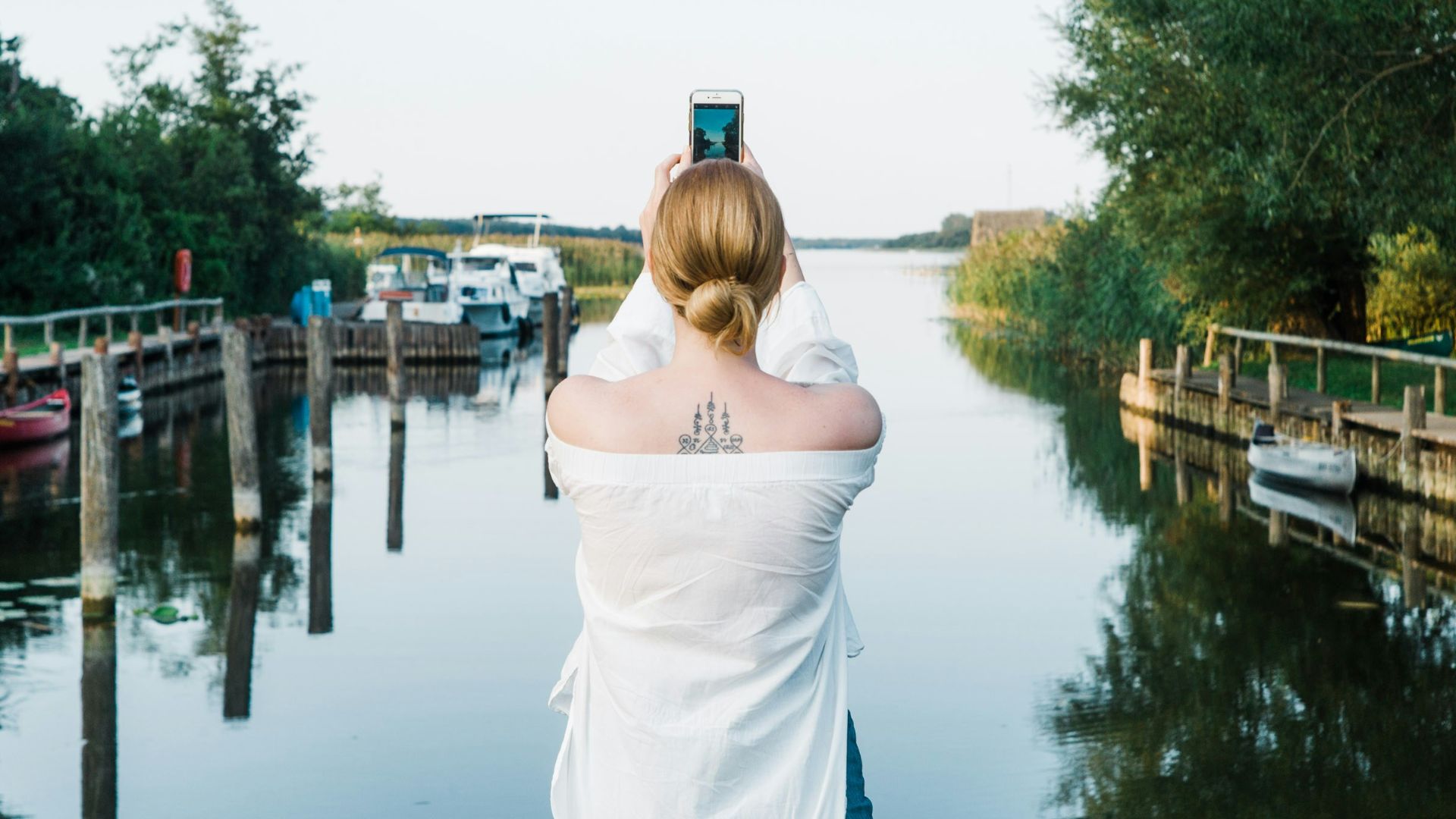 woman standing beside lake while holding smartphone