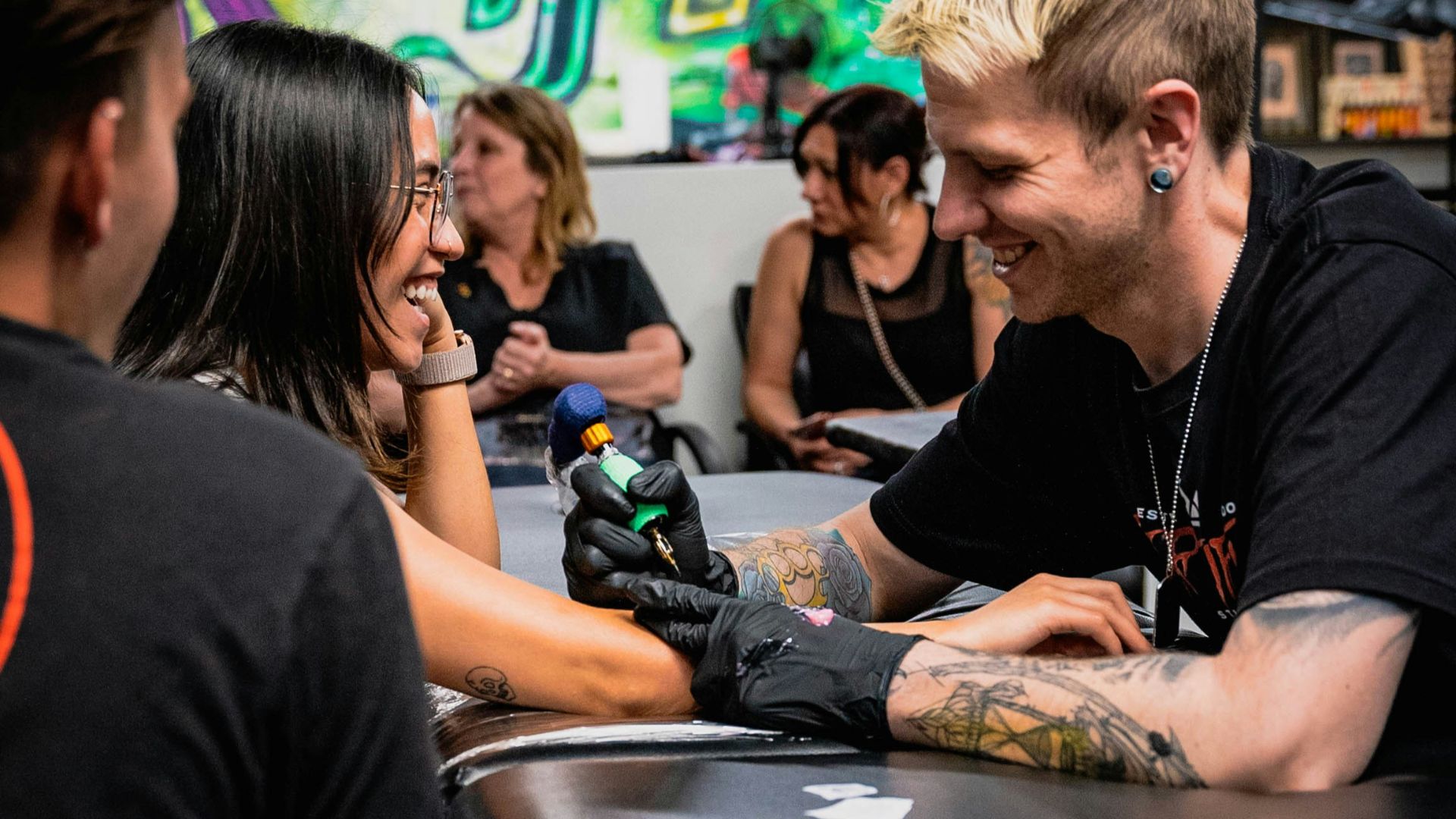 A tattoo artist inks a client's arm.