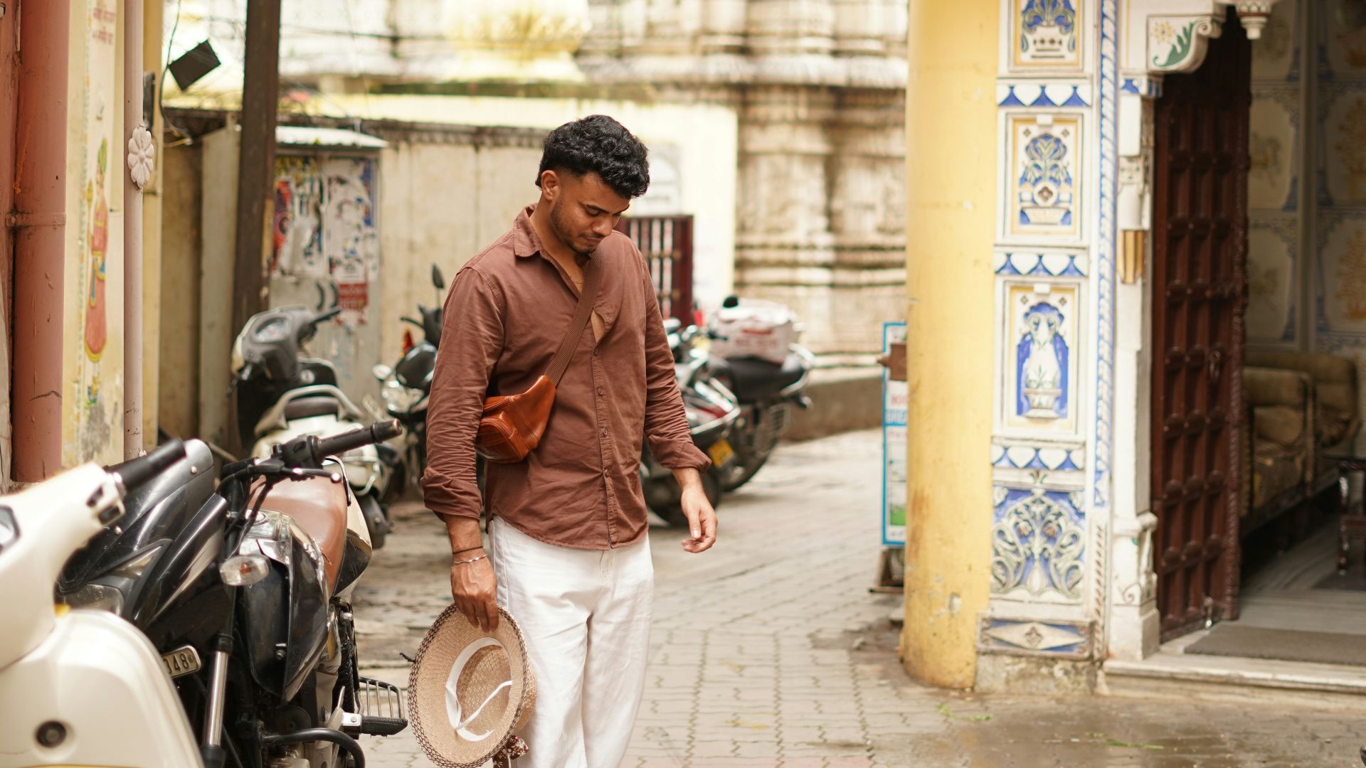 Man walks down a narrow alleyway with motorcycles.