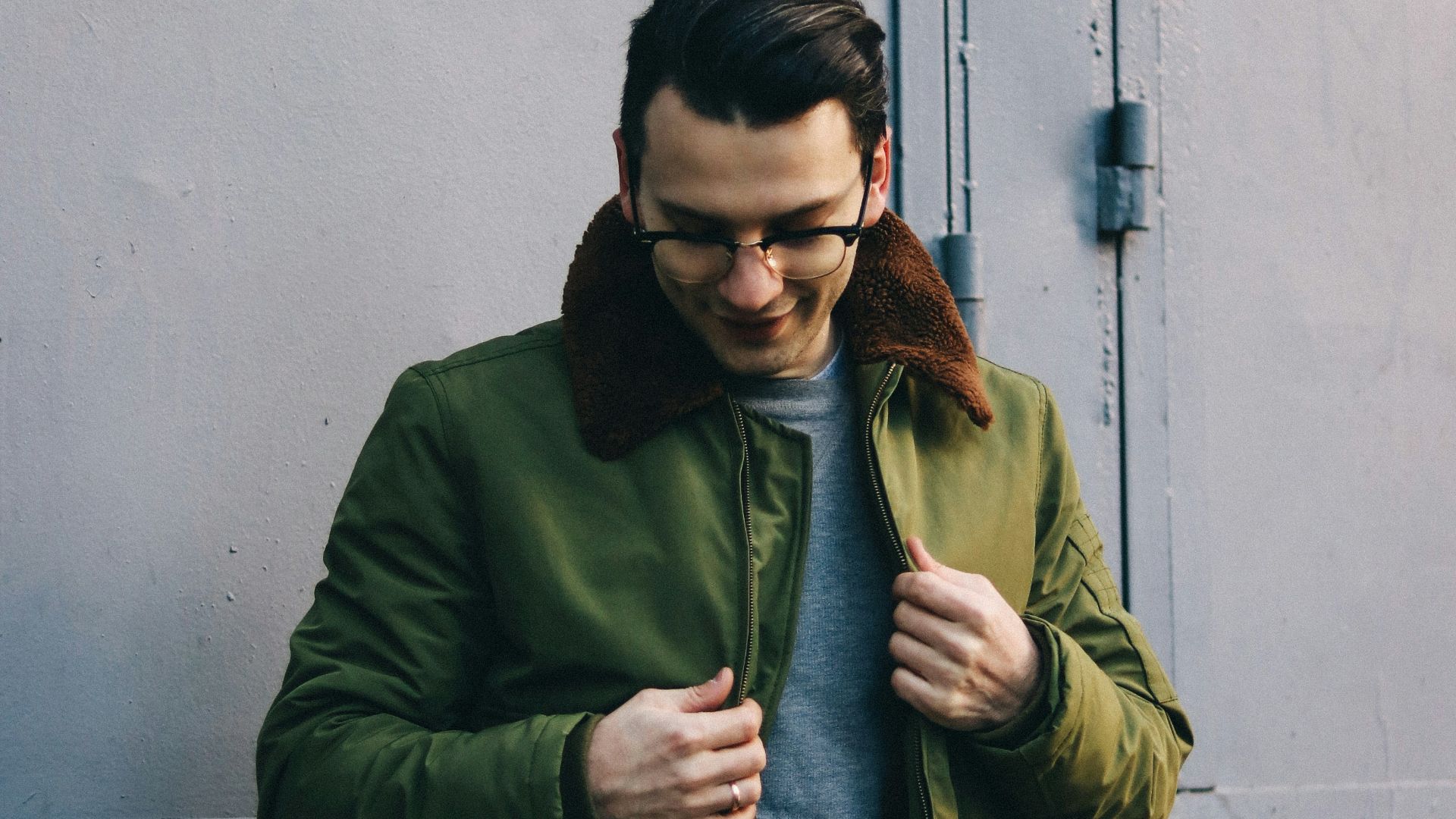 man in green jacket standing near white wall