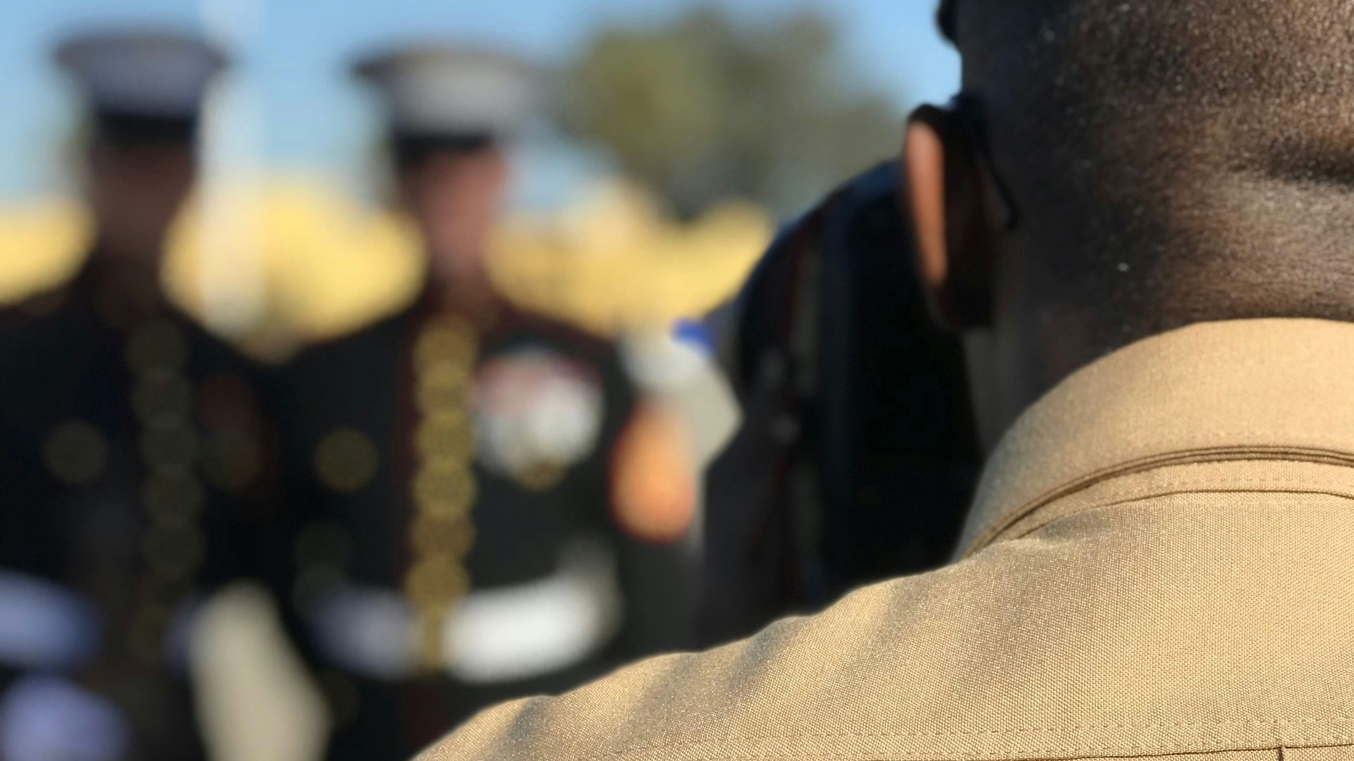 man in brown office uniform facing people in black officer uniform