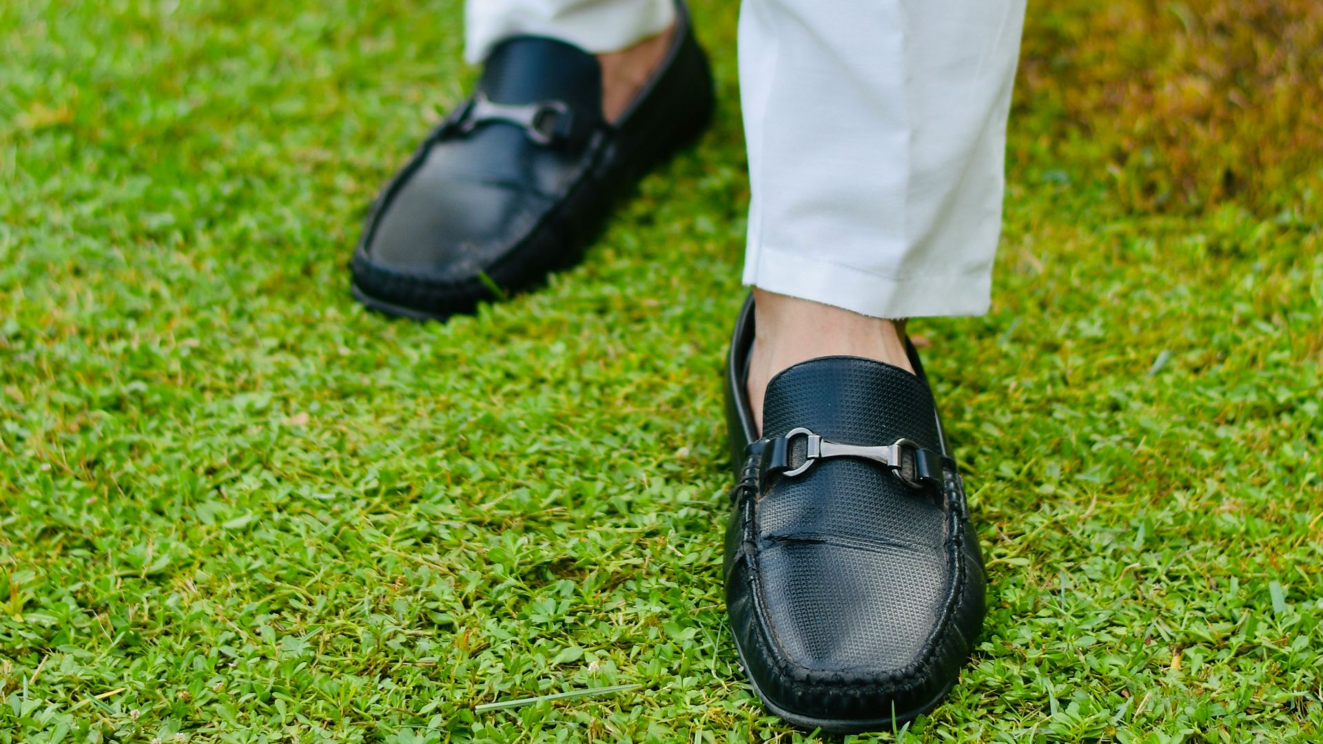 a person in white pants and black shoes standing on grass