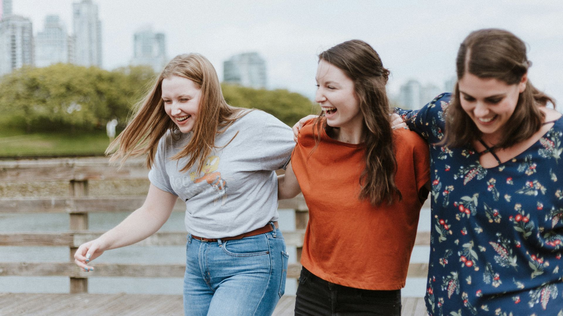 three women walking on brown wooden dock near high rise building during daytime