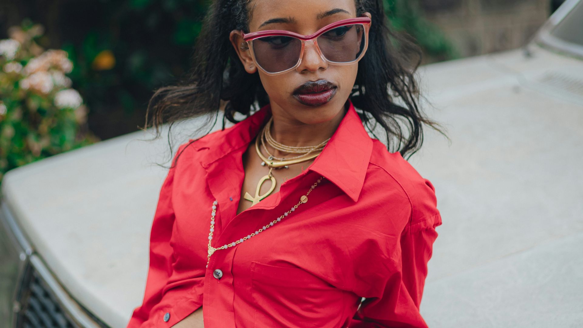 Stylish woman in red shirt leans on car