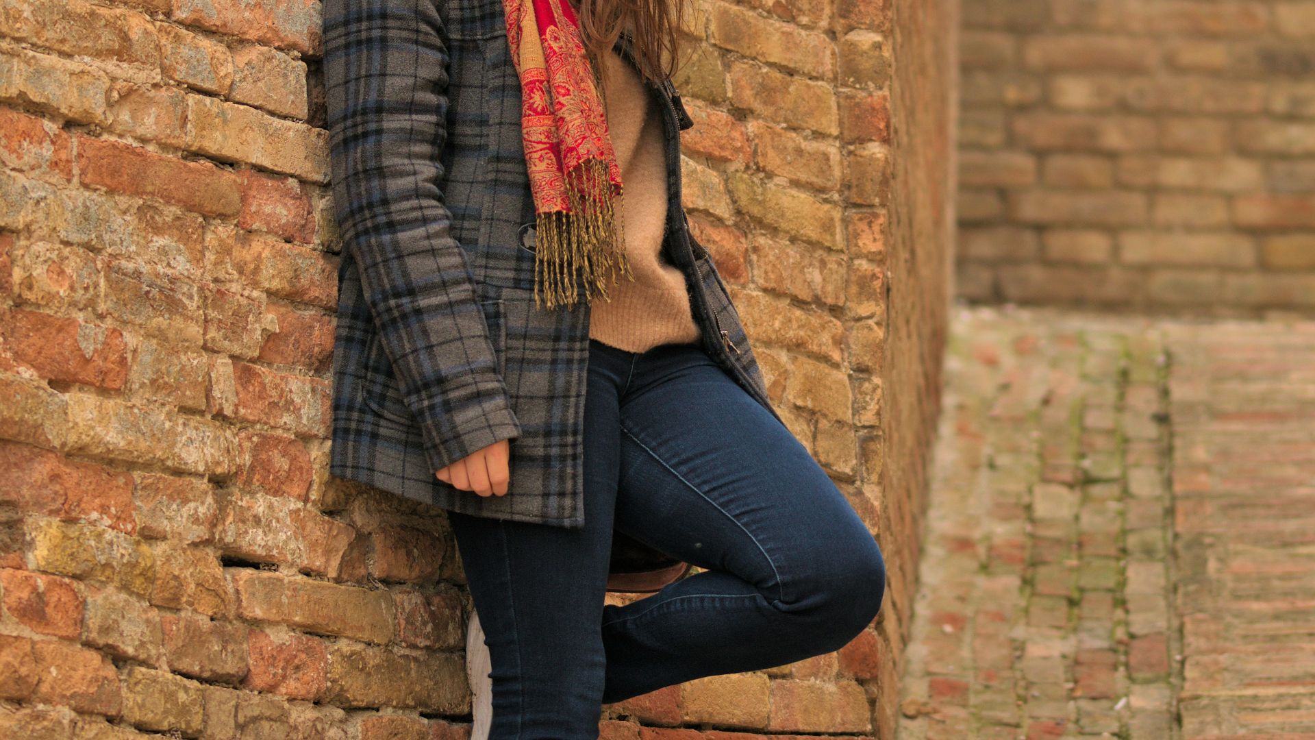 a woman leaning against a brick wall with a scarf around her neck