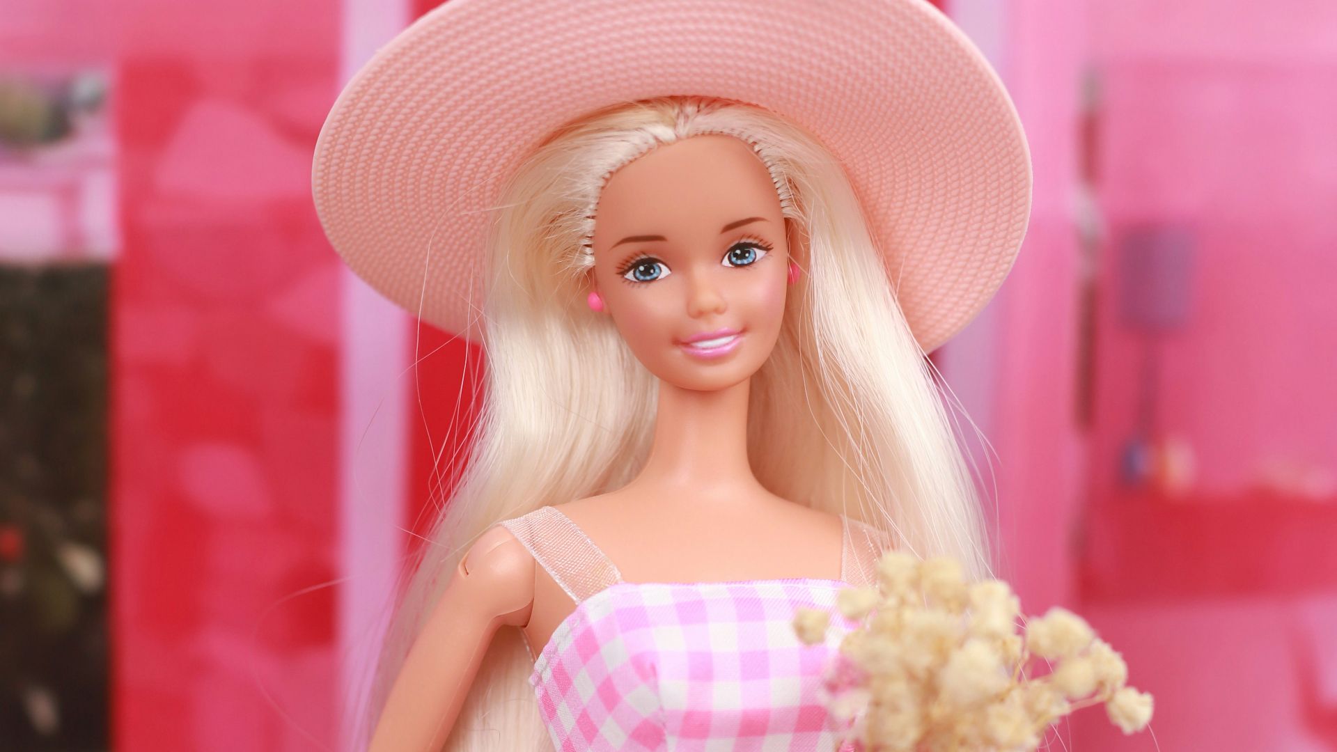 A barbie doll in a pink dress and hat on a pink motorcycle