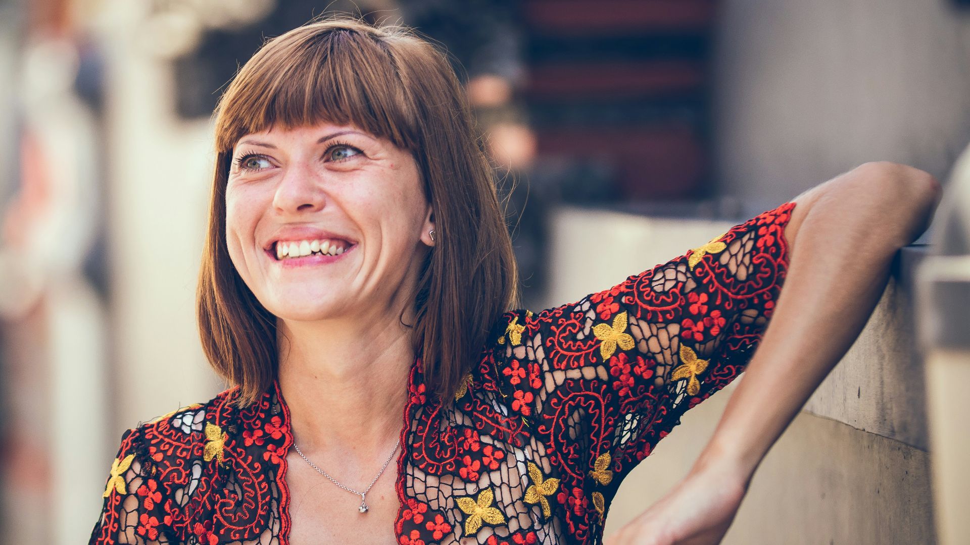 woman in floral-themed cardigan leaning on fence in bokeh photography