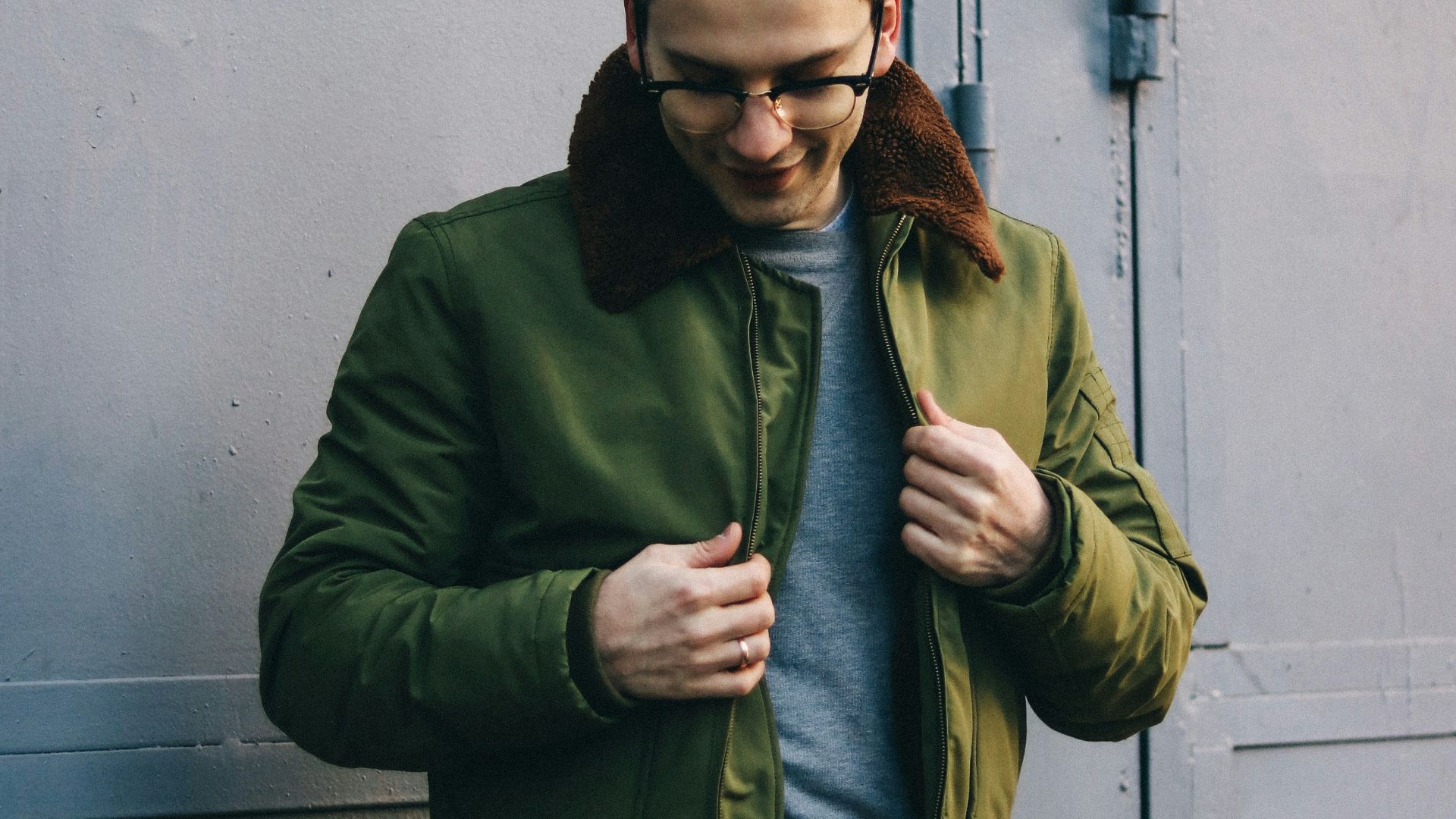 man in green jacket standing near white wall