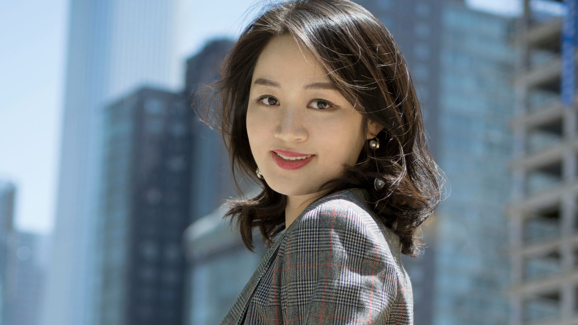 smiling woman wearing red, black, and gray plaid blazer