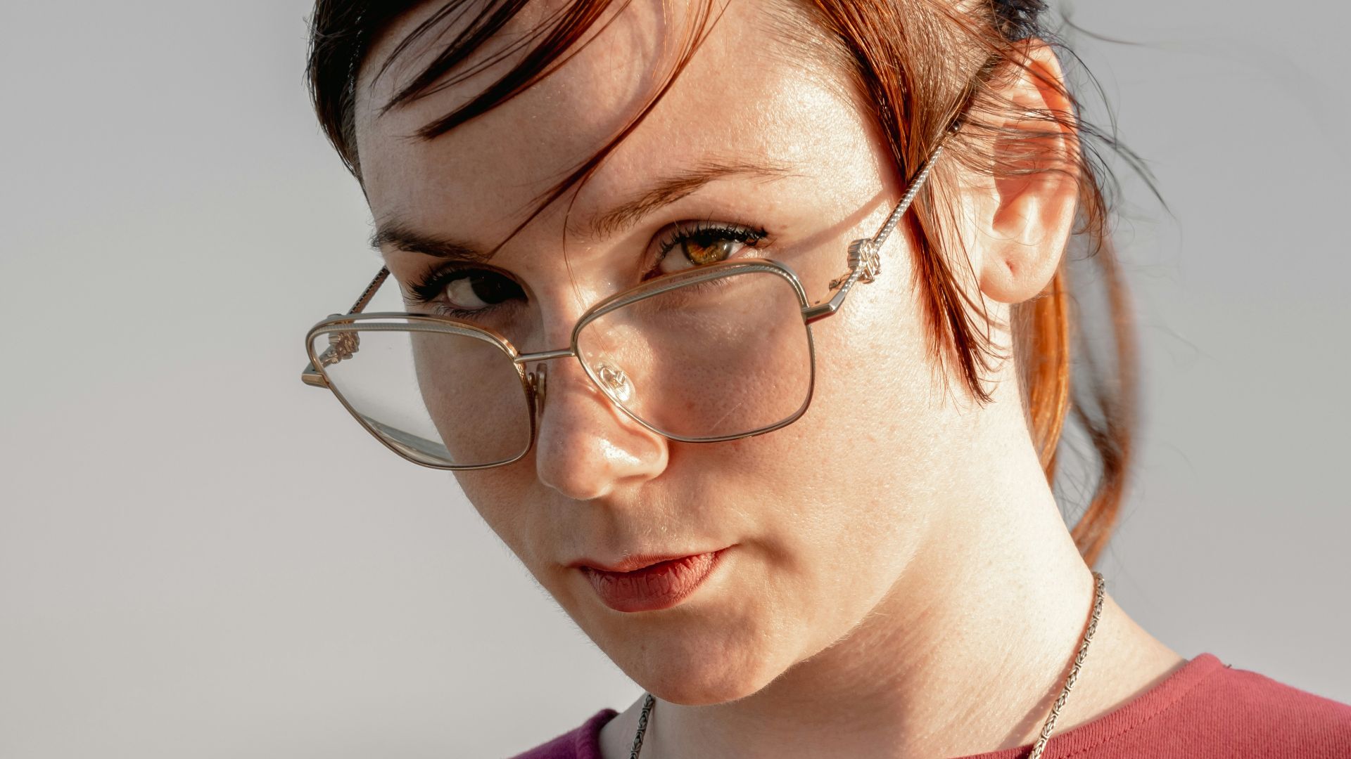 Woman with glasses and anchor necklace looks at camera