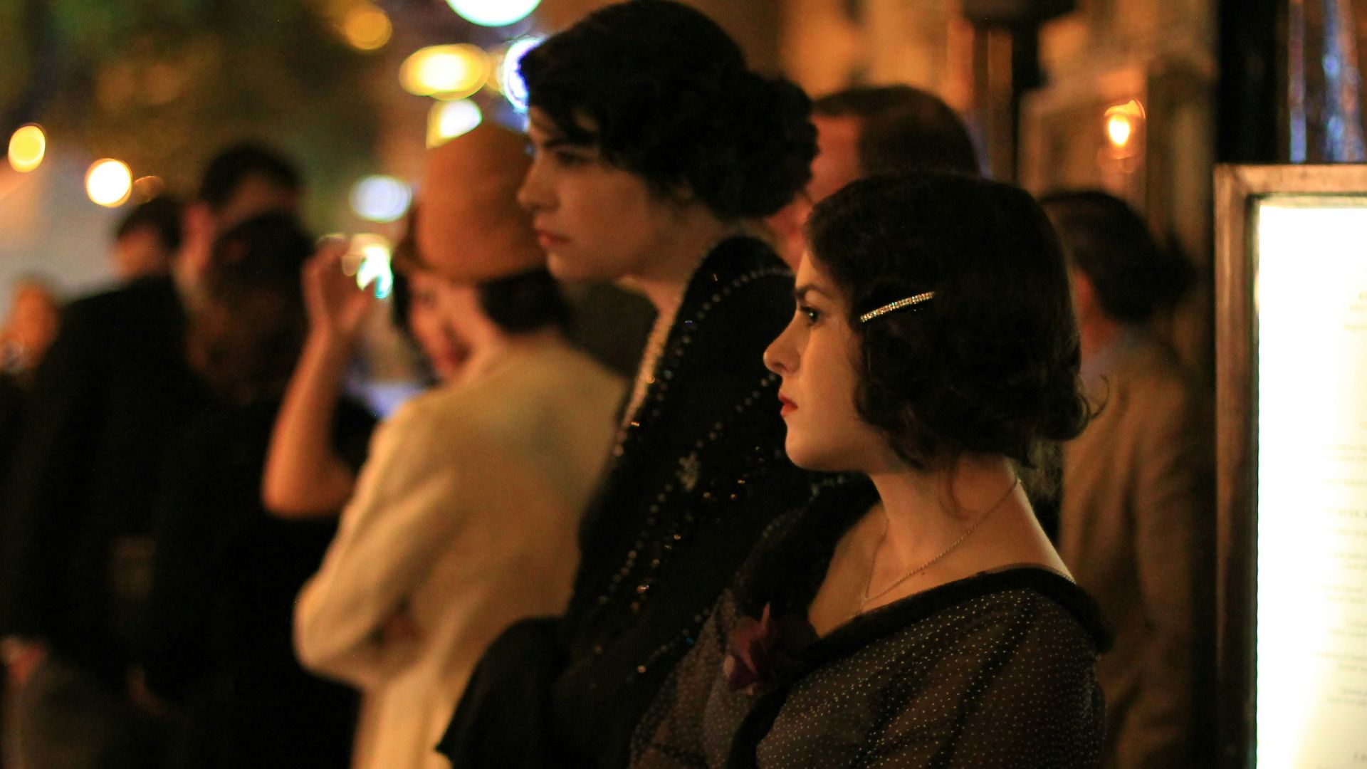 People in vintage clothing stand outside at night.