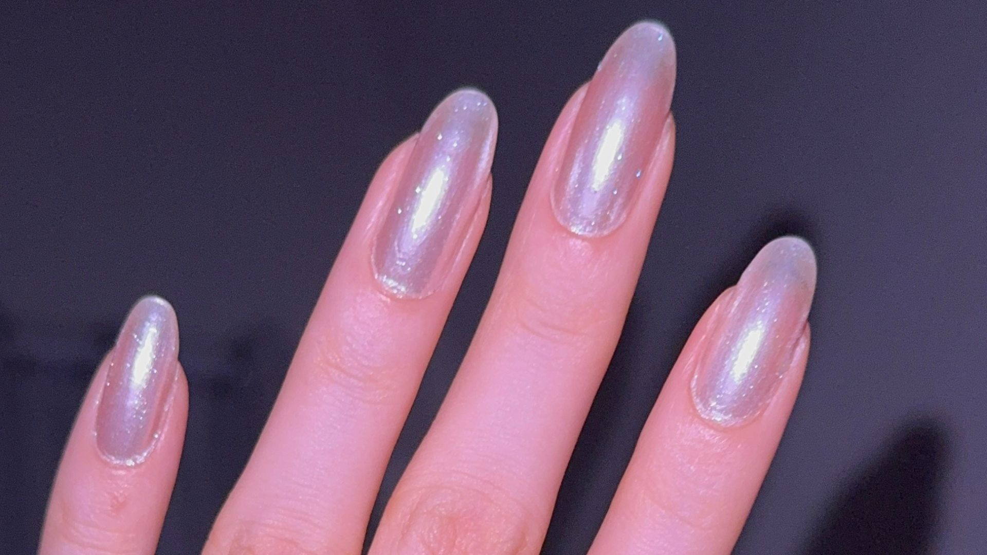 Hand with pearlescent nails and rings.