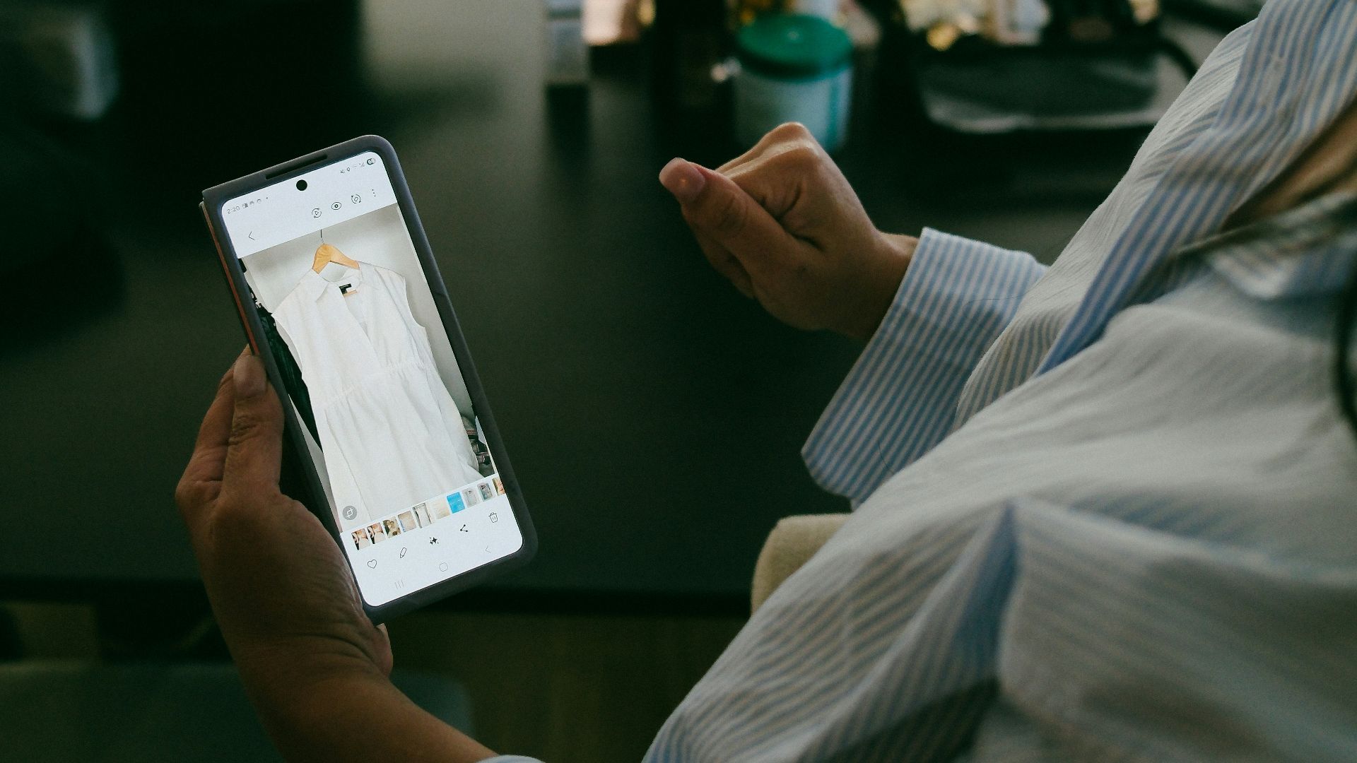 Woman holds phone showing white dress on screen.