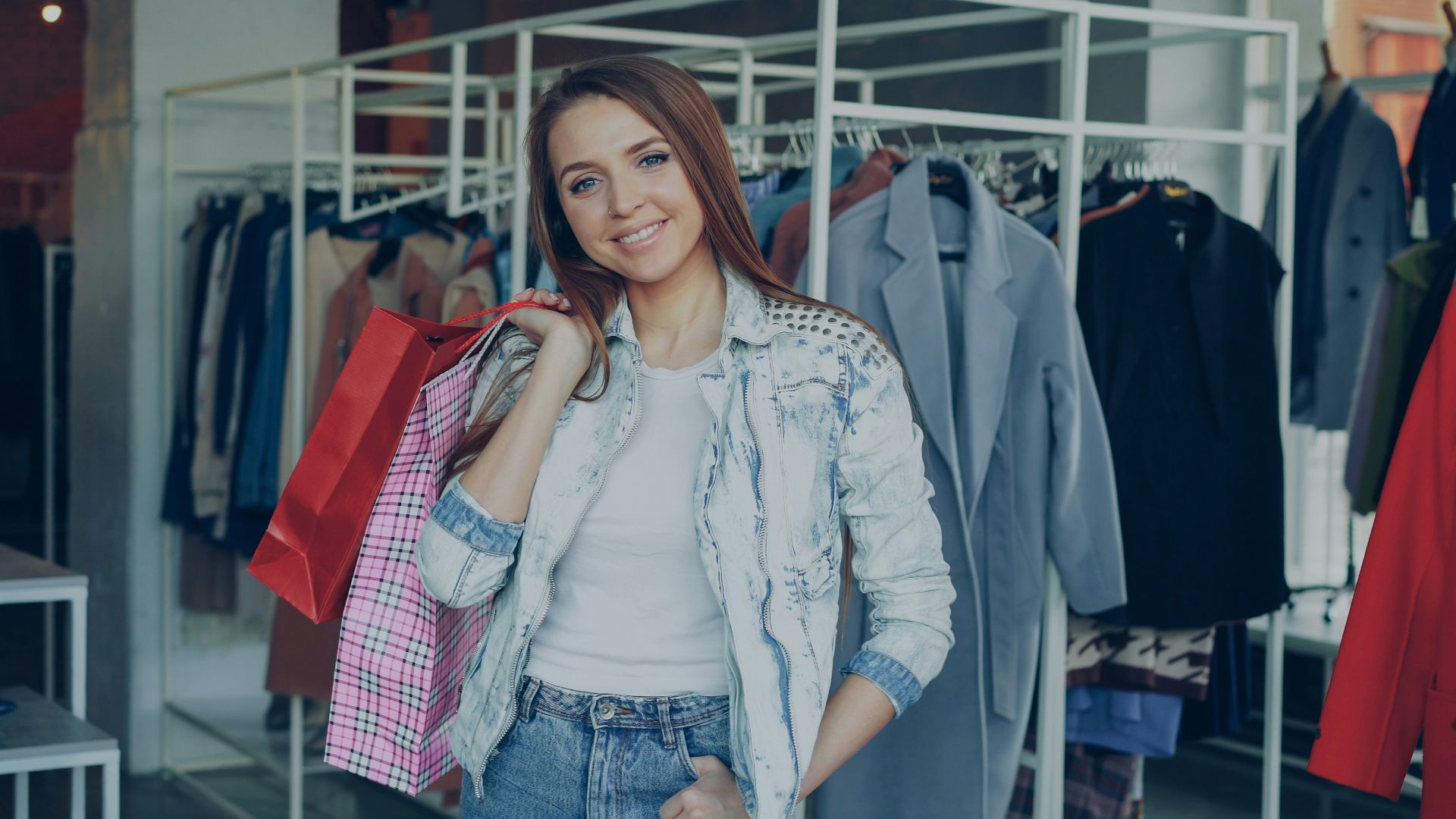 Woman smiles with shopping bags in a clothing store.