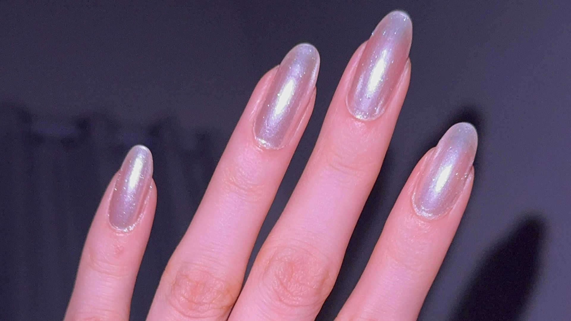 Hand with iridescent nail polish and rings.