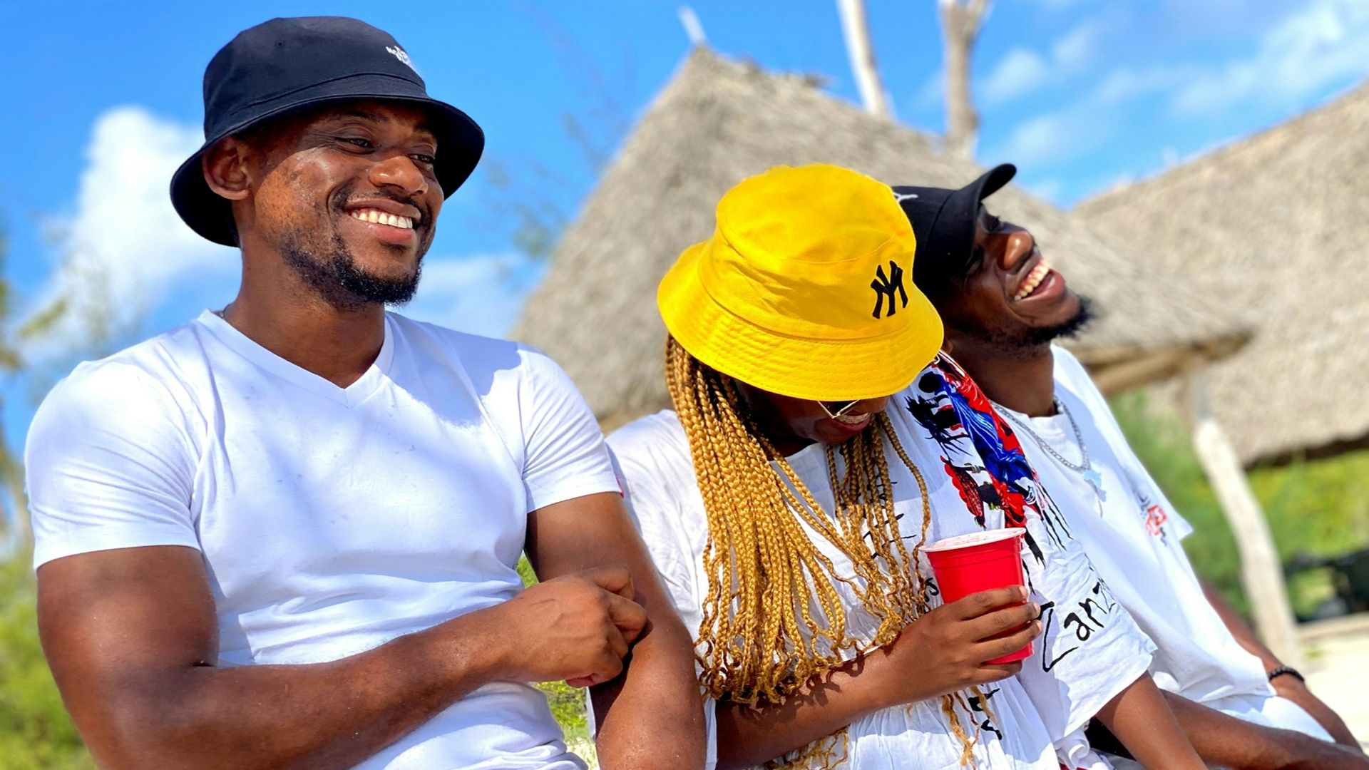 Three friends laughing together outdoors on a sunny day.